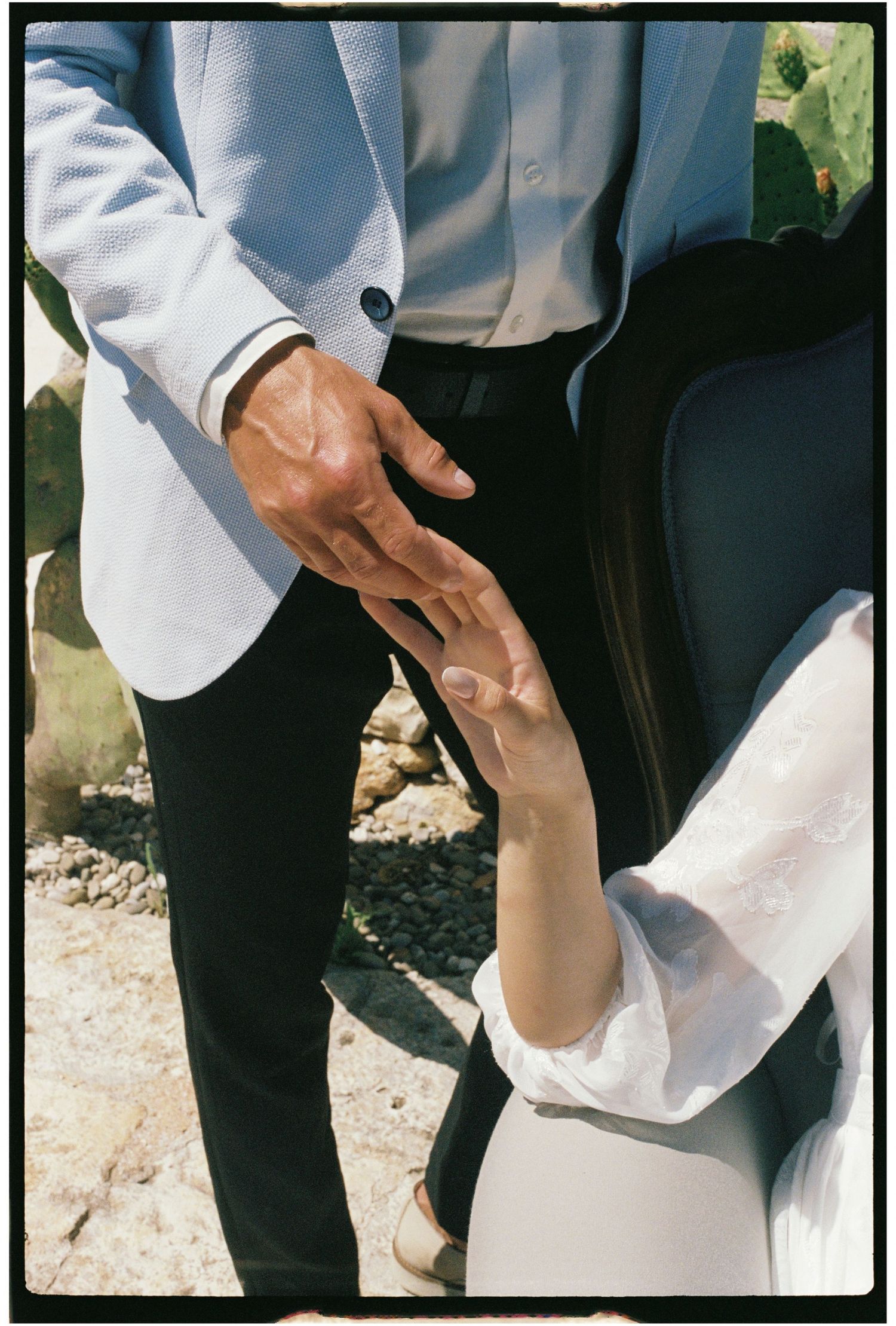 Close-up of bride and groom holding hands outdoors on a sunny wedding day.