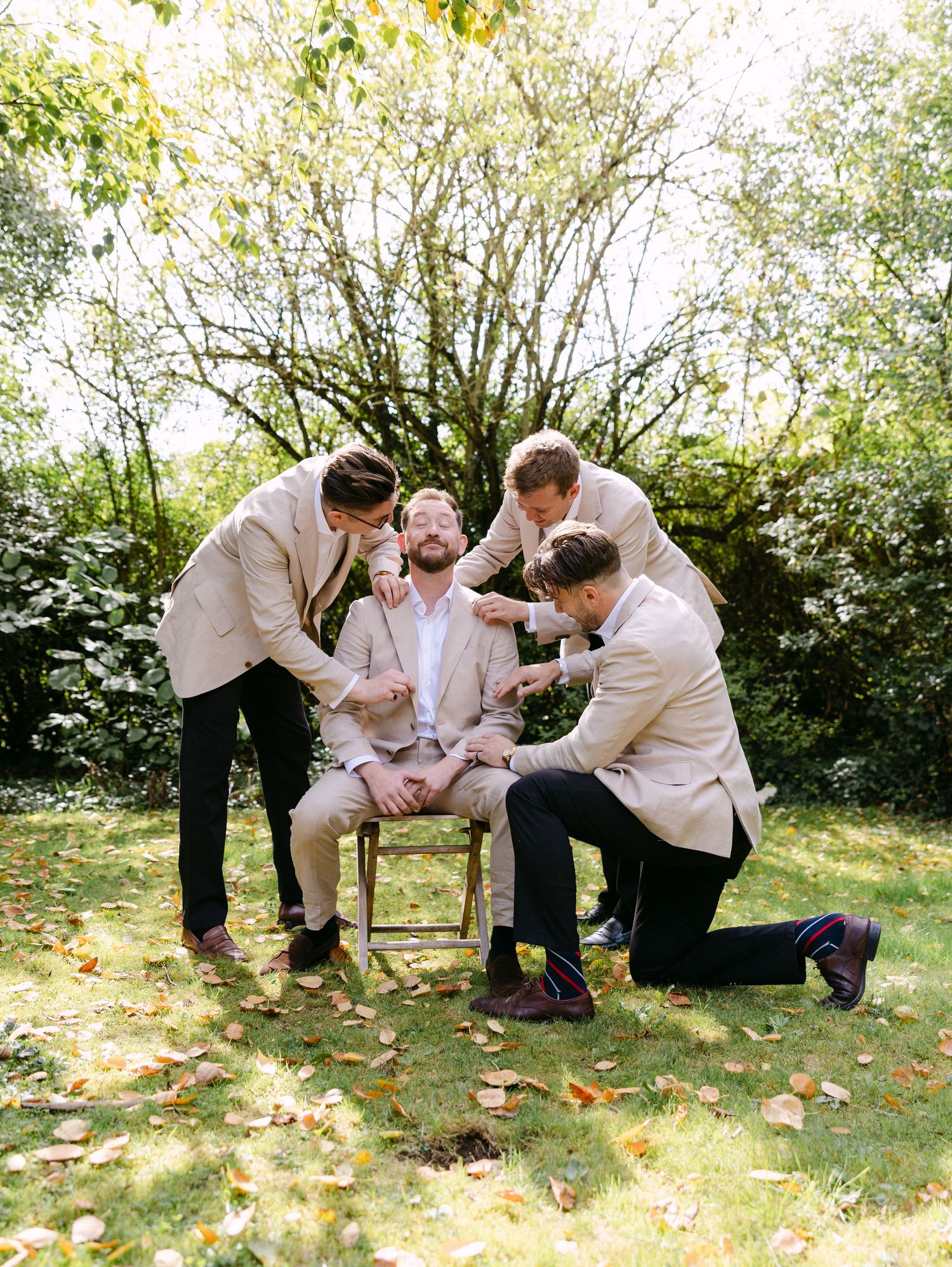 Group in white suits playfully posing on grass with autumn leaves.