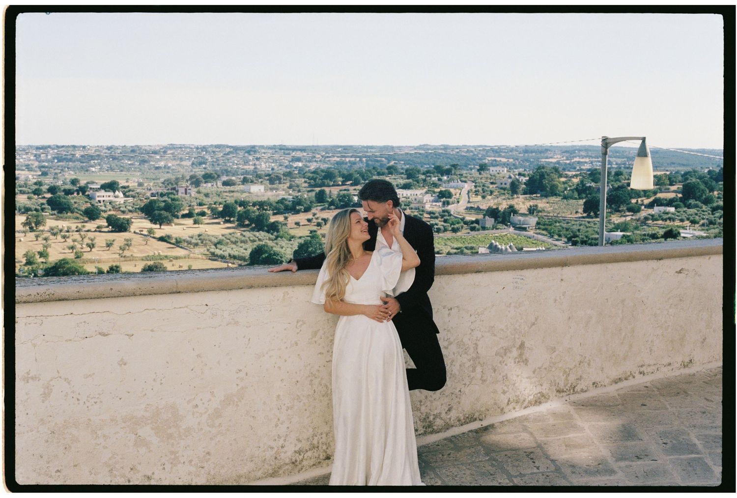 Wedding couple kissing on a rooftop terrace with panoramic Italian countryside views behind them.