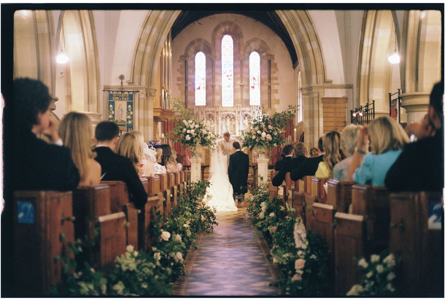 Elegant church wedding ceremony with floral aisle decorations and guests seated in wooden pews.