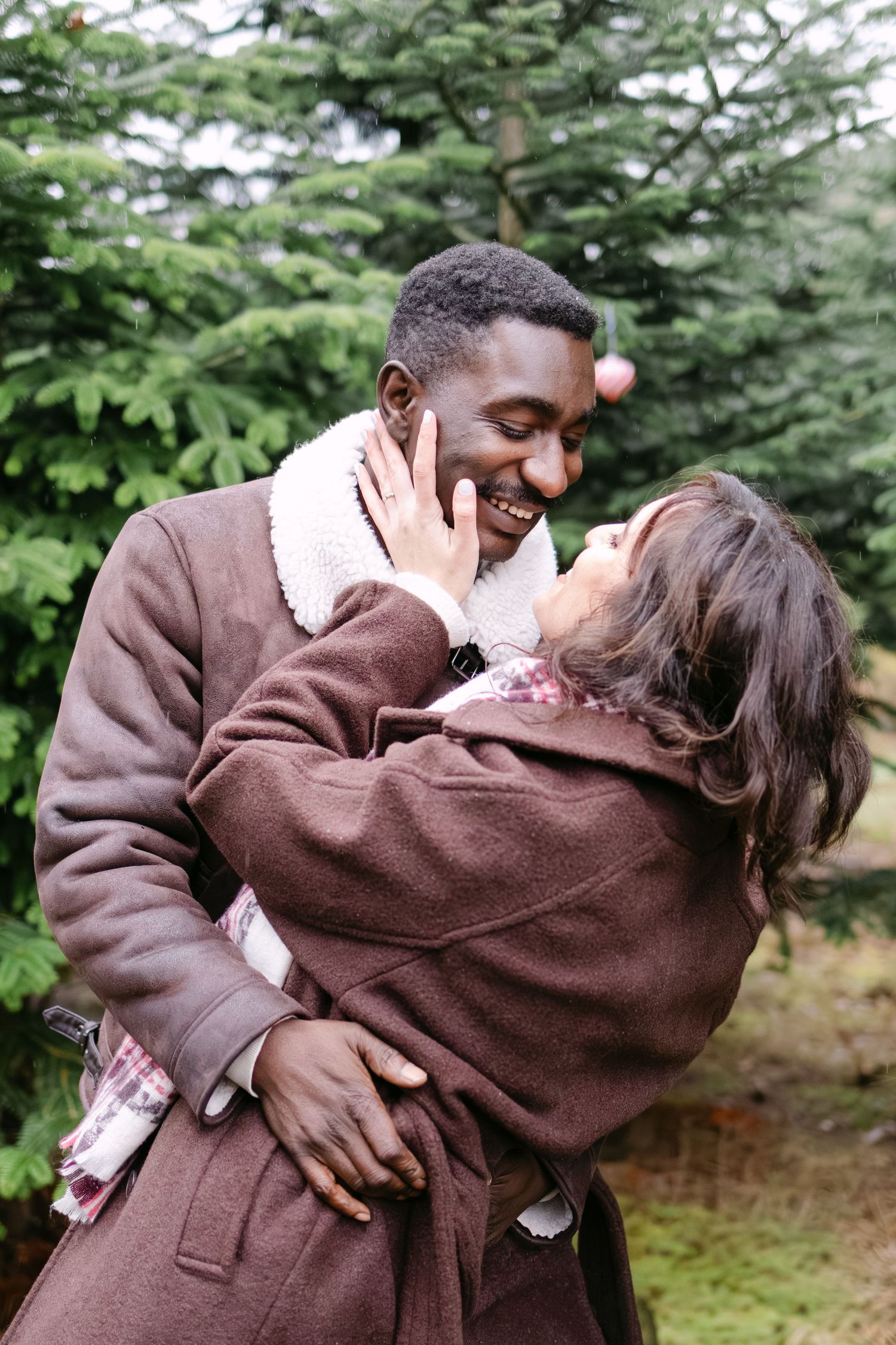 A couple embraces warmly in a series of romantic photos outdoors against an evergreen forest backdrop.