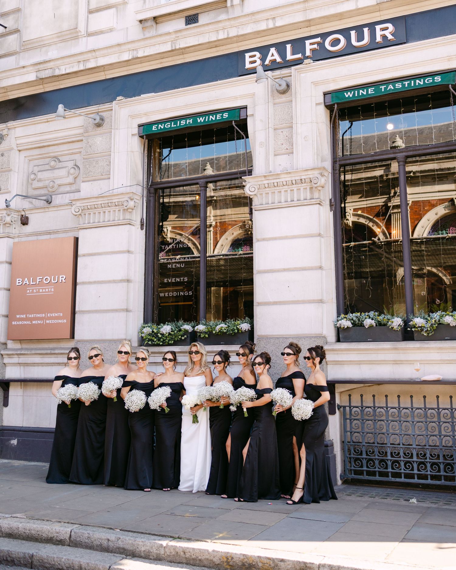 Wedding party in black and white attire posed in front of the Balfour restaurant storefront.