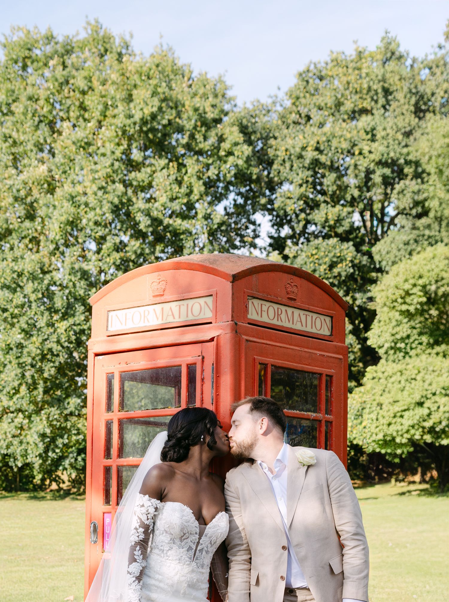 A romantic moment shared in front of a classic red British telephone booth surrounded by lush greenery.