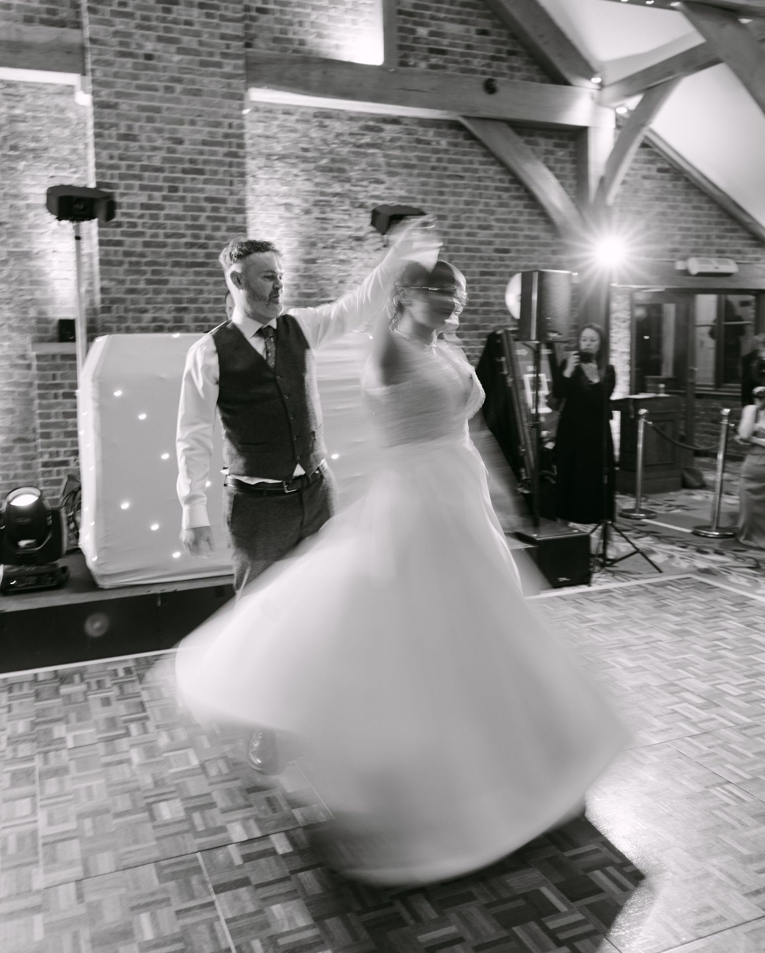 Black and white photo of a bride twirling in her wedding dress during the first dance at a rustic barn venue.