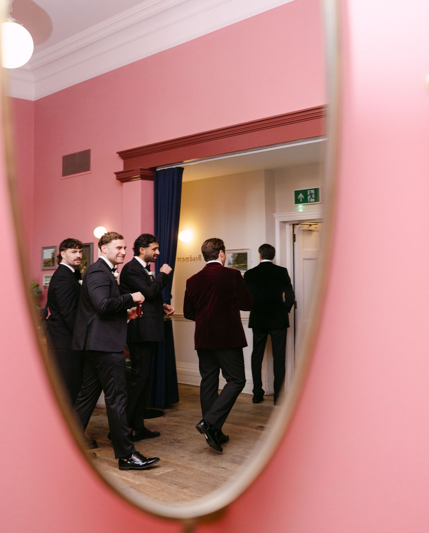 Reflection of formal event guests in a round mirror mounted on pink walls.