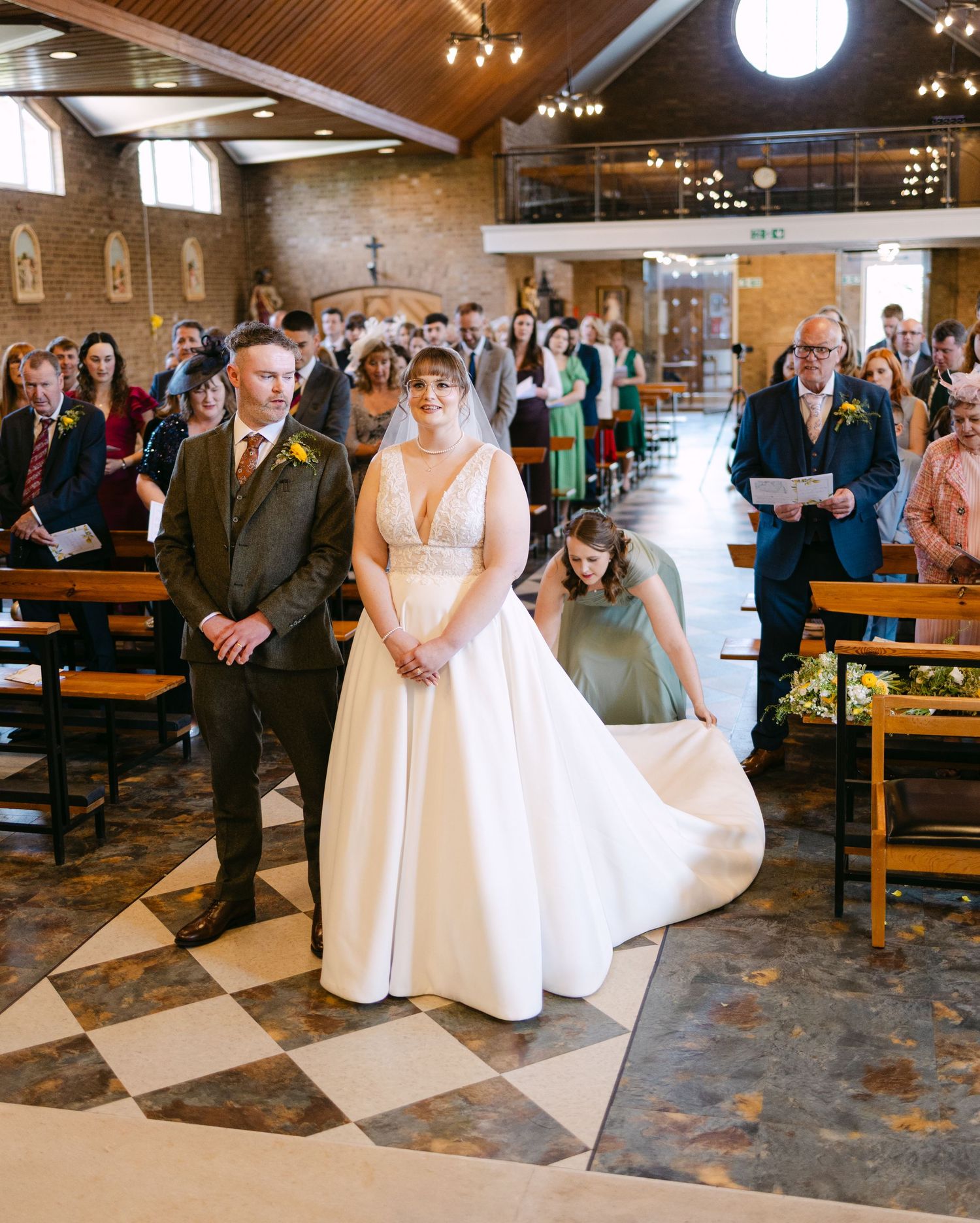 Bride and groom stand at the altar in a church wedding ceremony, with guests seated in wooden pews and a flower girl nearby.