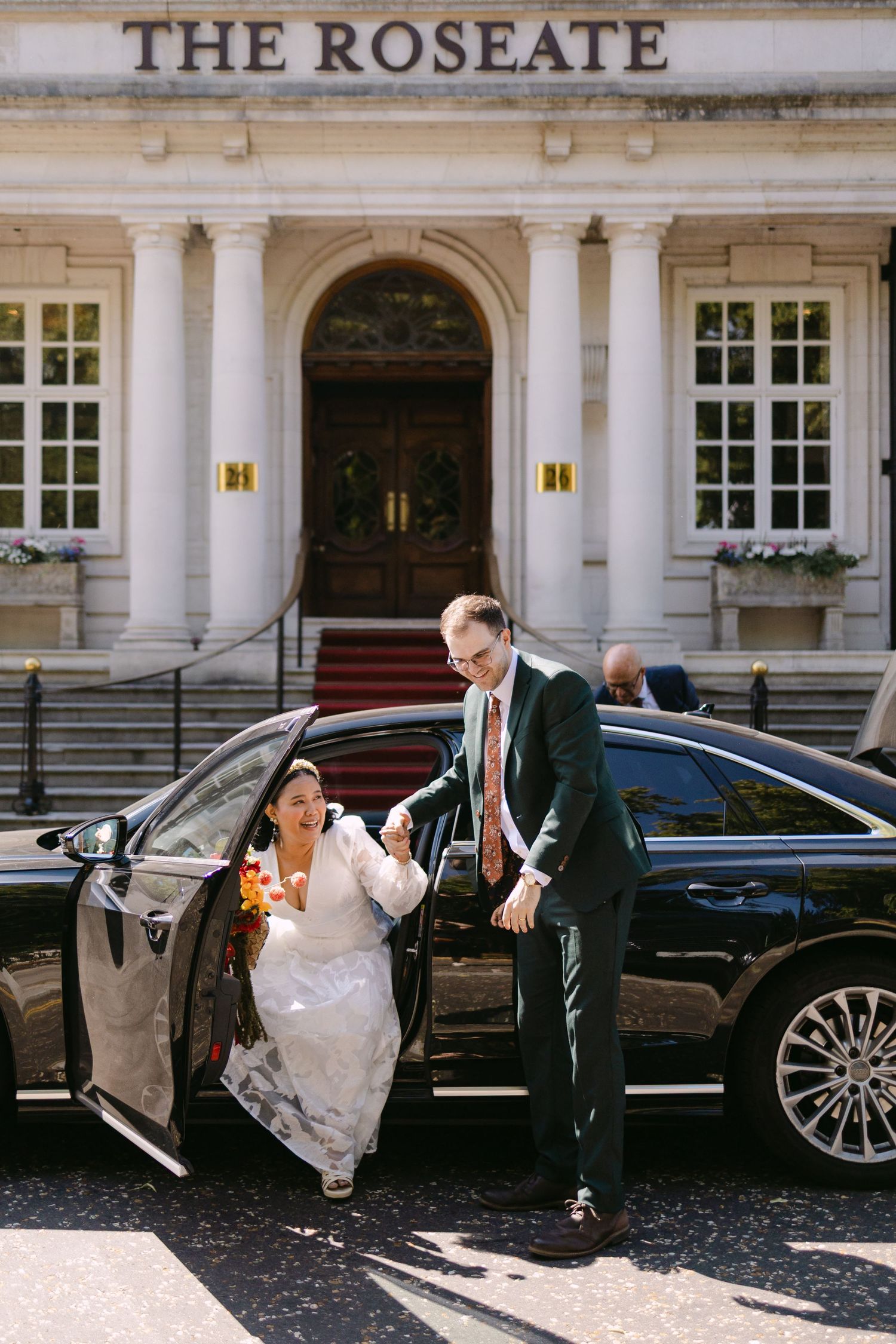 Bride and groom arriving at The Roseate hotel, stepping out of a black luxury car on their wedding day.