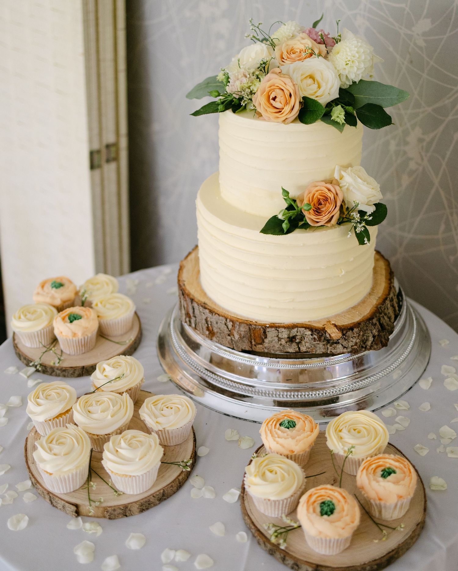 White wedding cake with peach roses displayed alongside matching cupcakes.