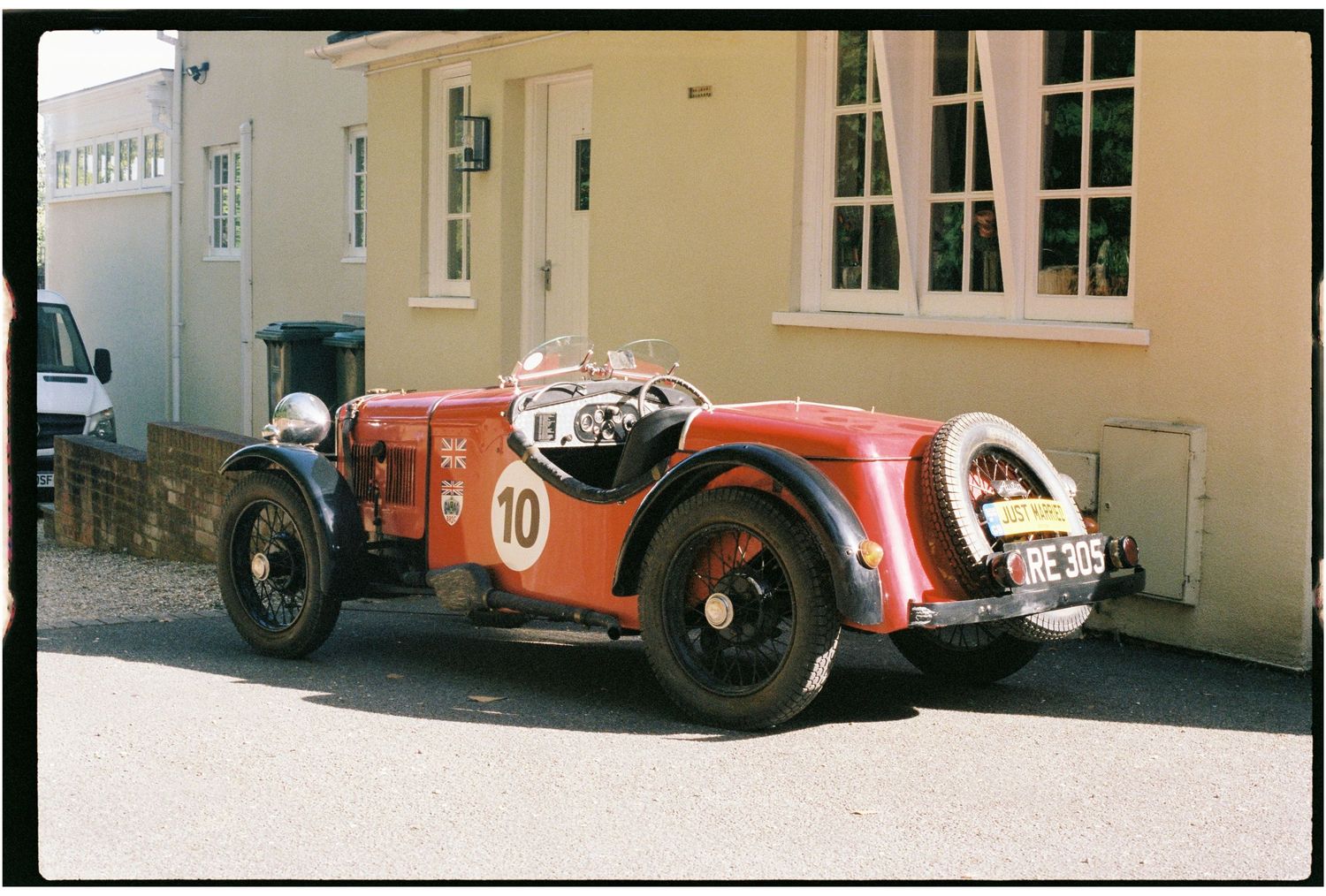 Vintage red racing car number 10 parked on a street beside a white building.