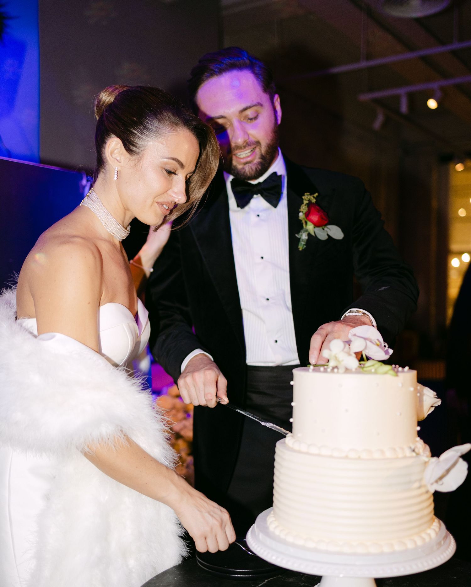 Bride in white dress and groom in tuxedo share a moment while cutting their wedding cake.