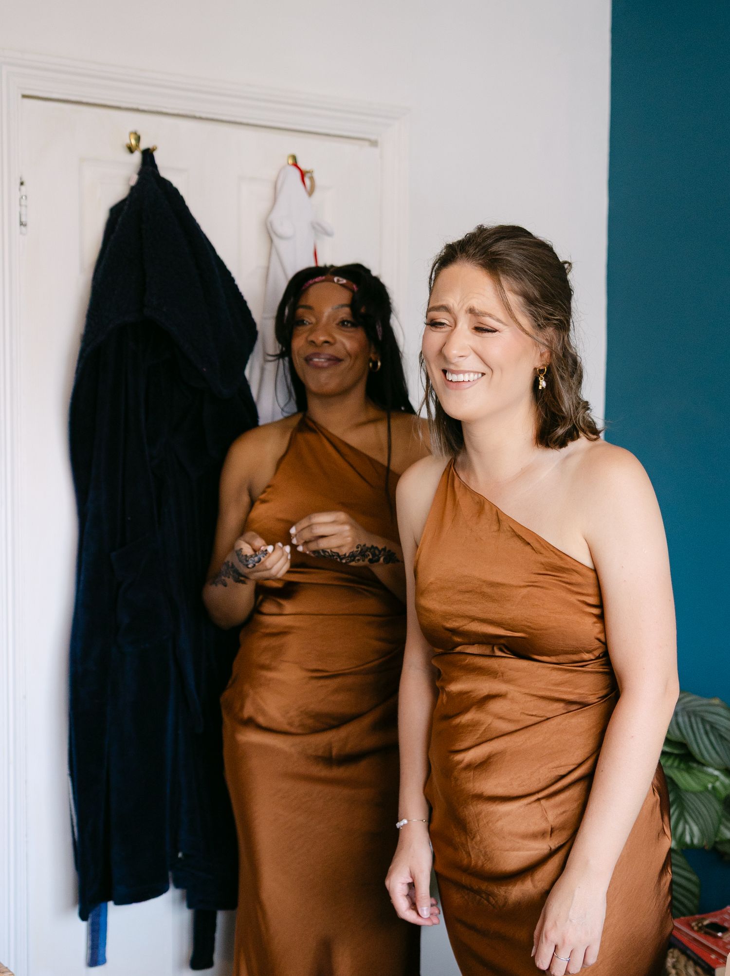 Two people in copper-colored dresses sharing a candid moment indoors.
