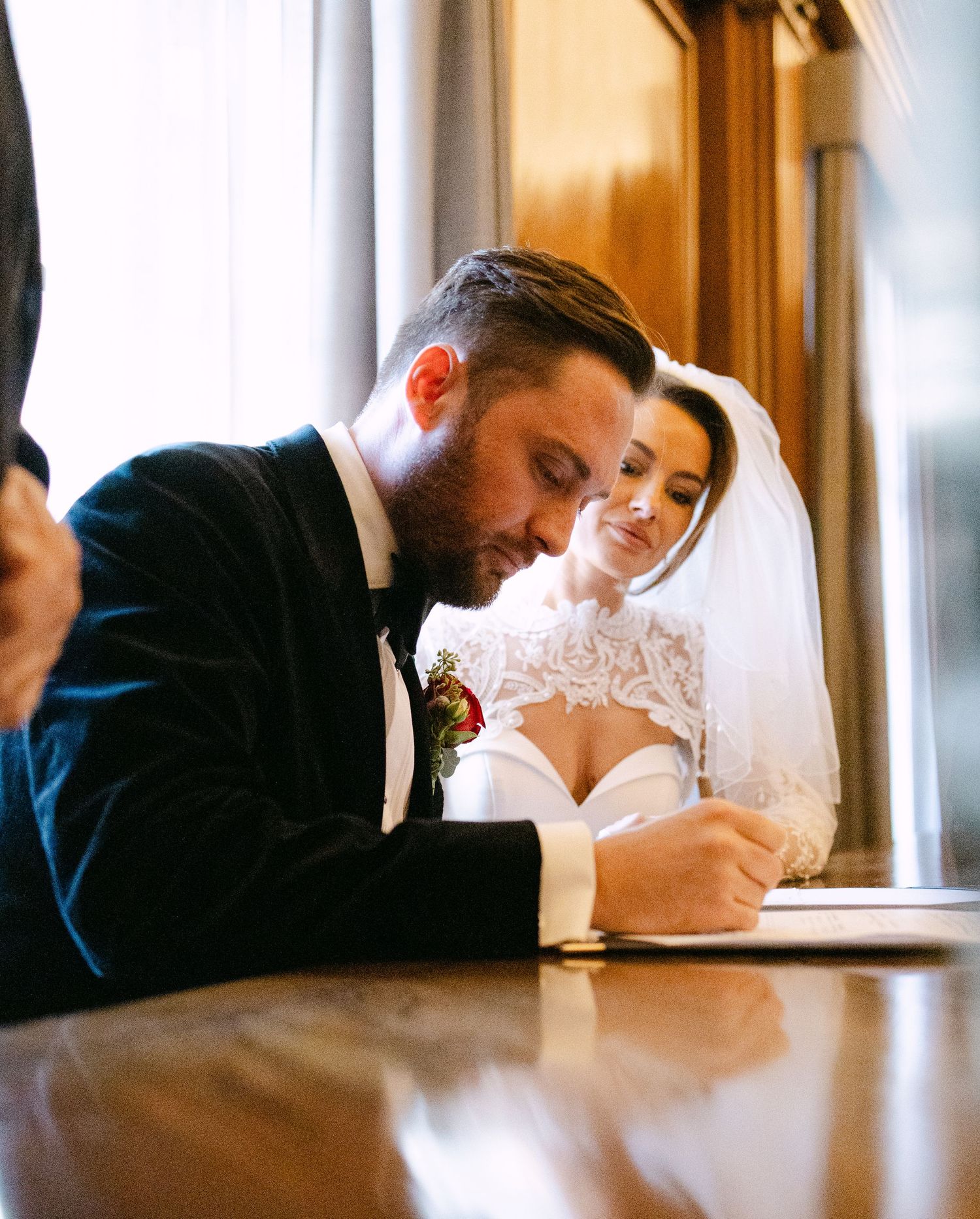 Wedding couple signs documents at a wooden table during their marriage ceremony.