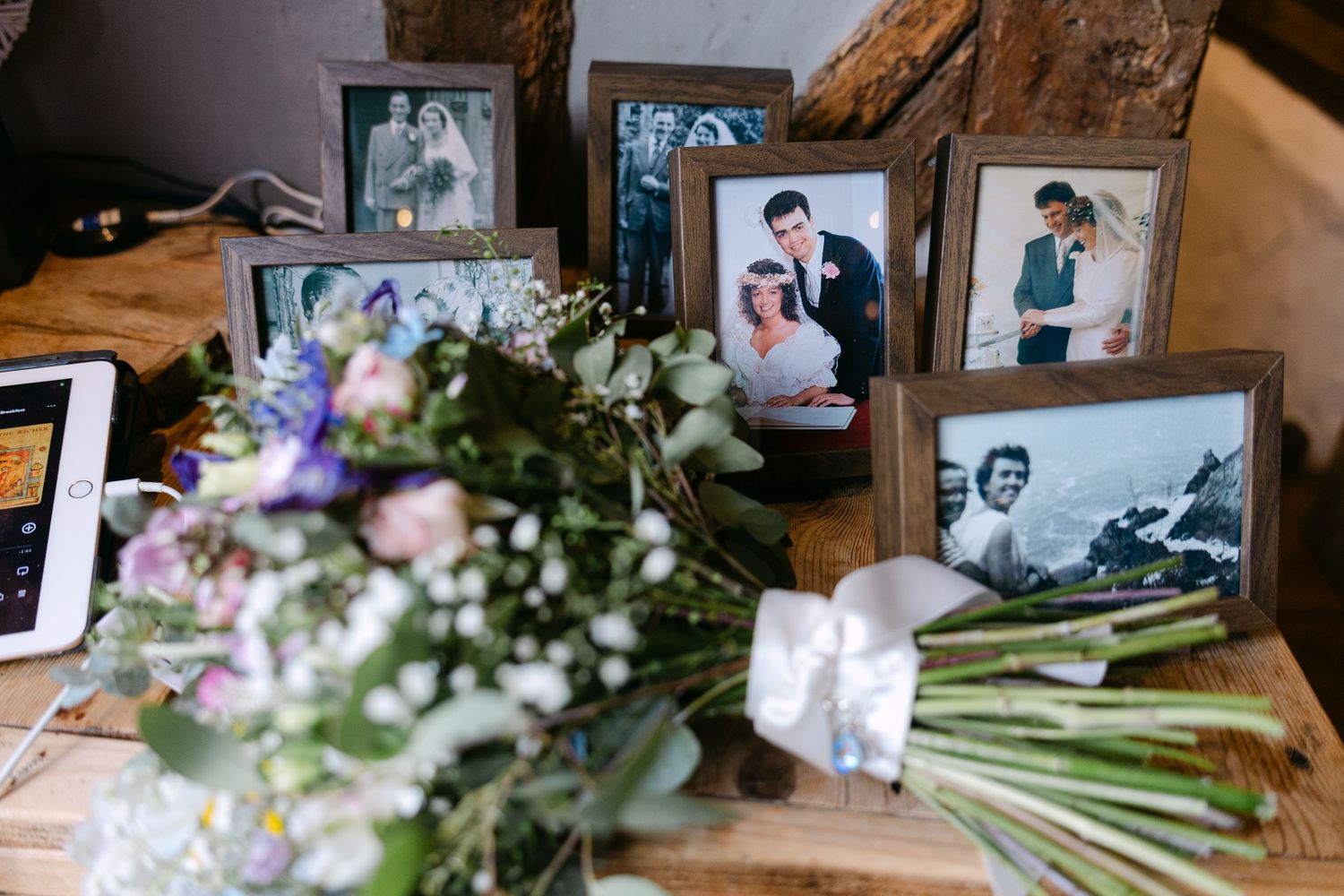 Framed vintage wedding photos displayed on a wooden table with a bouquet of fresh flowers in soft purple and white hues.