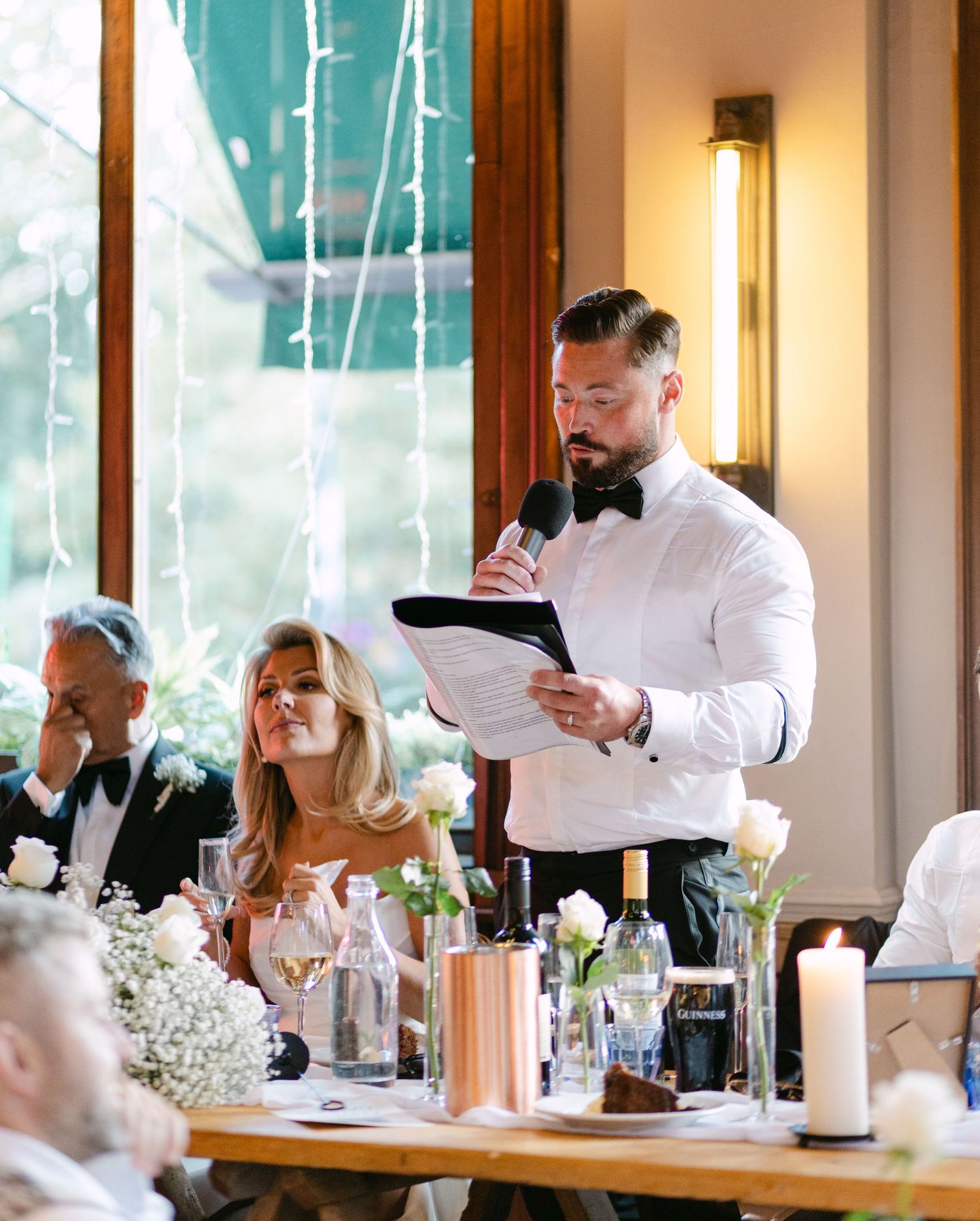 A guest delivers a speech while standing at the wedding reception table.