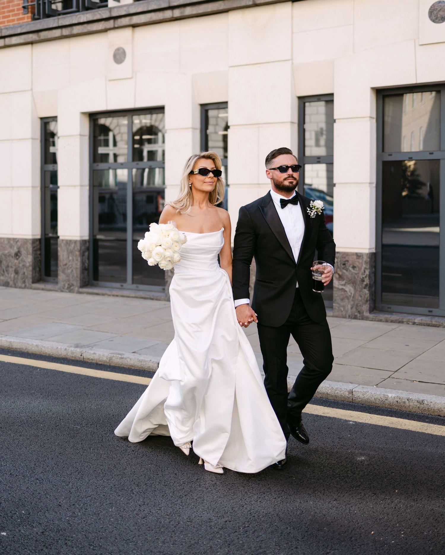 Elegant couple walks together on city street during wedding photoshoot.