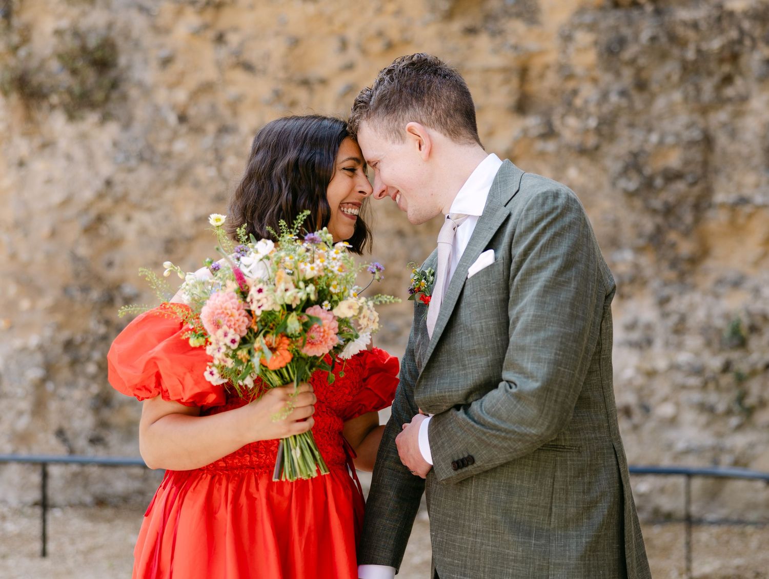 Newlyweds embrace against a rustic stone wall background during their wedding portraits.