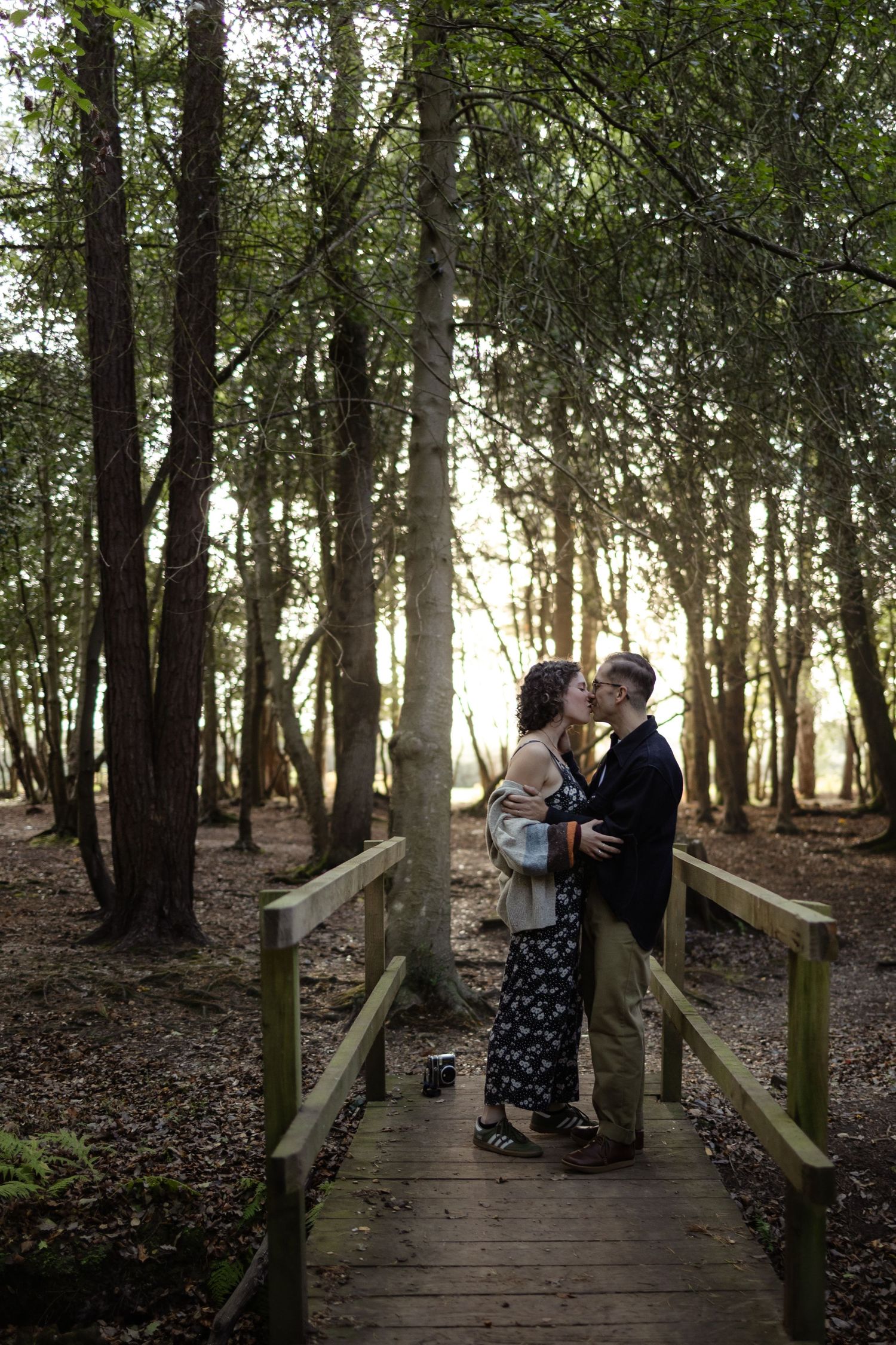 A couple sharing romantic moments on a wooden boardwalk surrounded by trees.