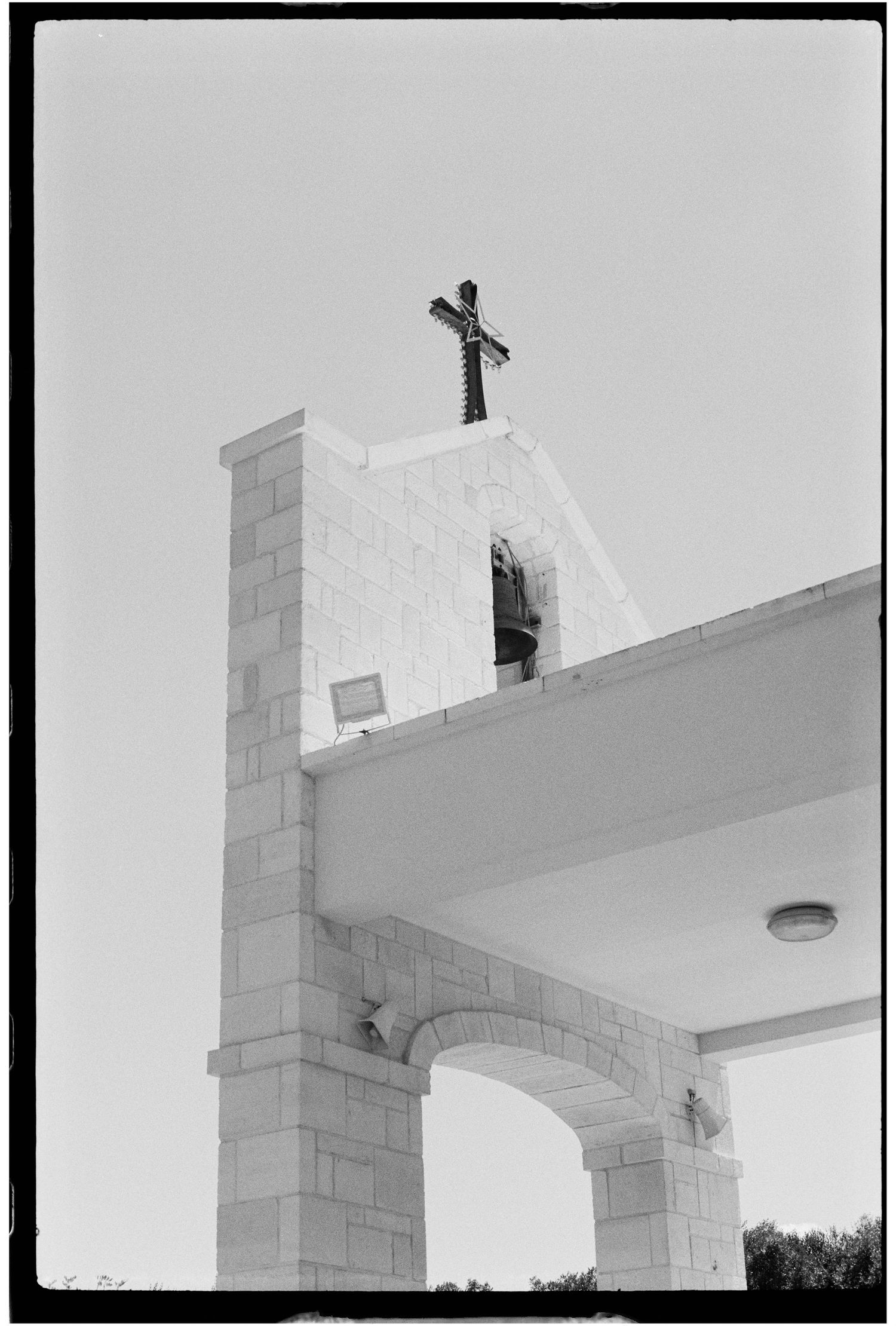 Black and white photo of a white stone church bell tower with a cross against a clear sky.