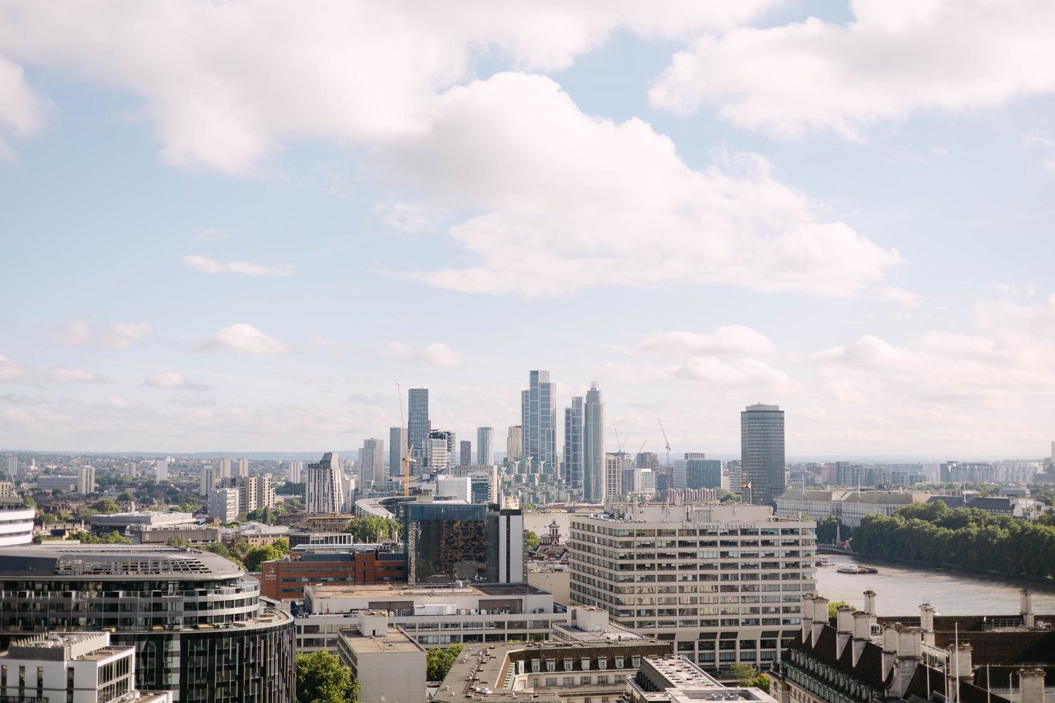 Aerial view of London cityscape with modern skyscrapers under a partly cloudy sky on a sunny day.