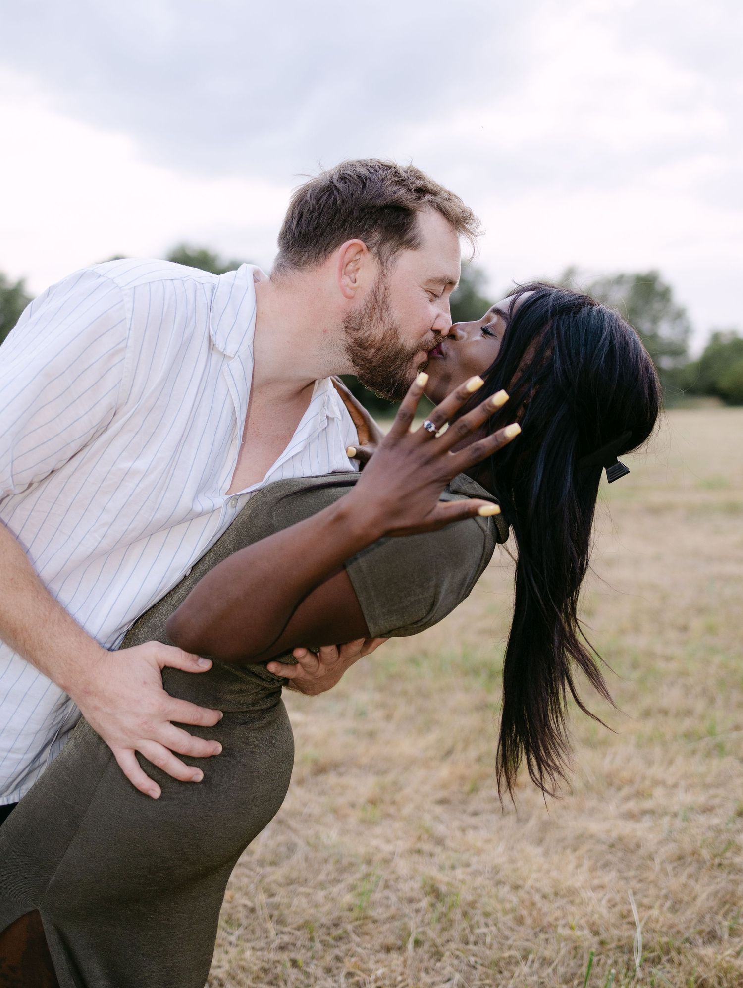 A couple shares tender kisses and embraces in a grassy field during a romantic outdoor photoshoot.