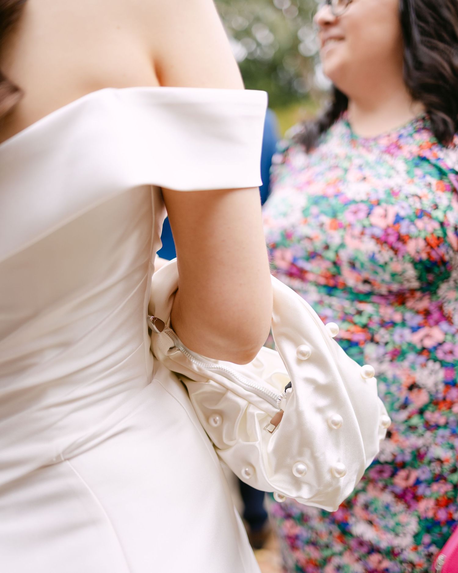 Close-up of white wedding dress details with floral print bridesmaids dresses in background.