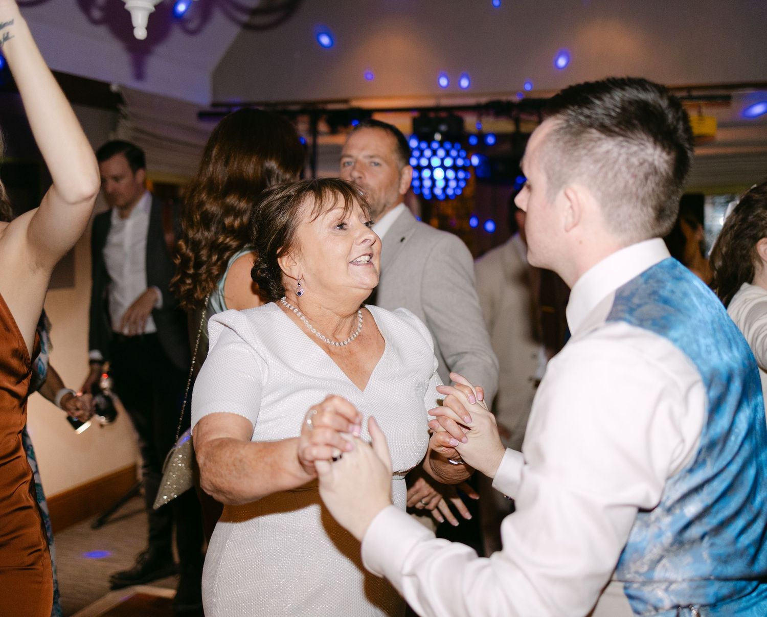 Wedding reception dance floor filled with guests dancing and celebrating under blue lights.