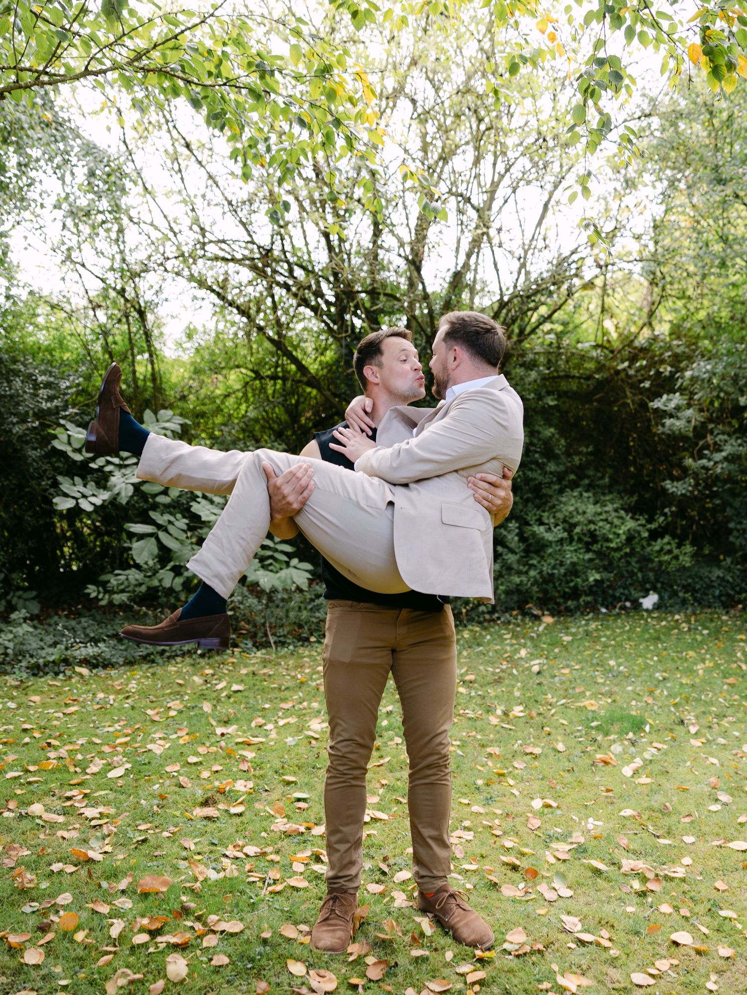 Couple in matching outfits sharing romantic moment in garden with fallen leaves.