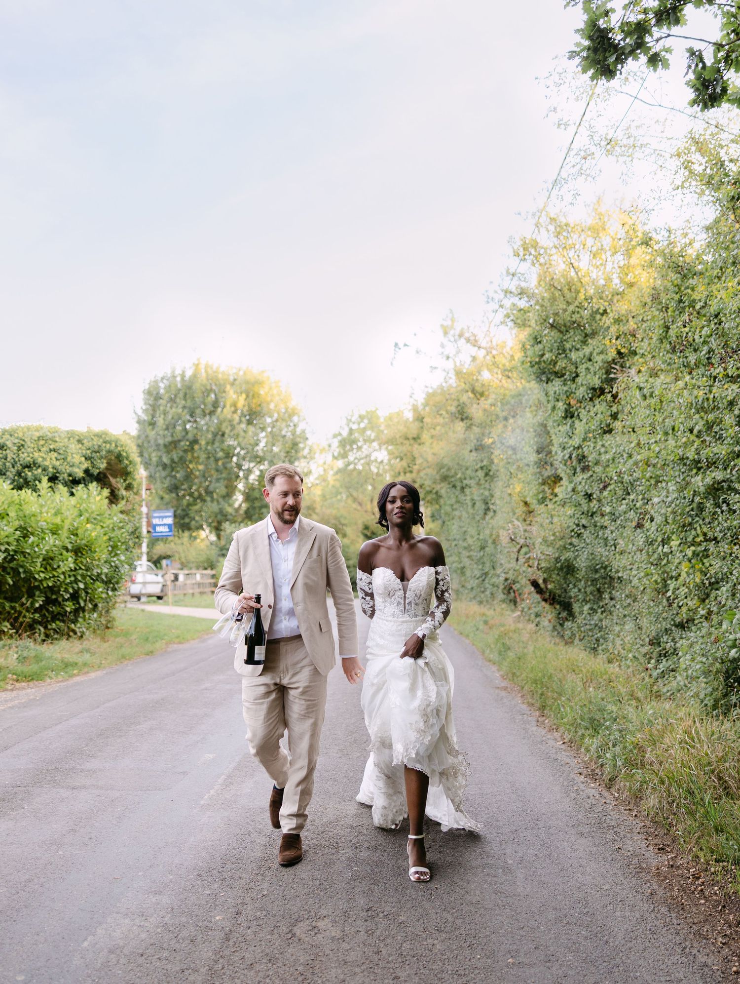 A couple walks down a country road together in wedding attire during golden hour.