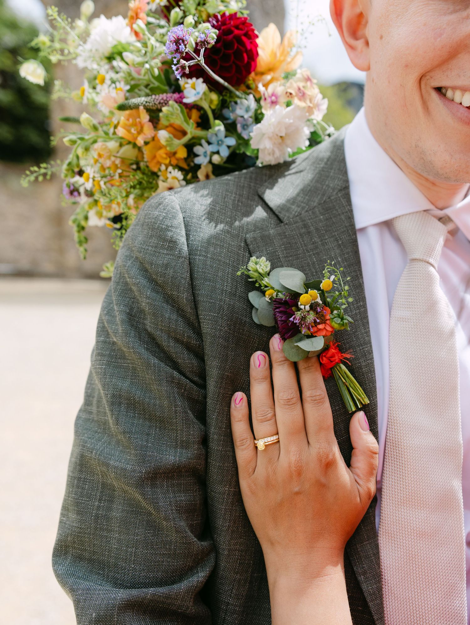 Close-up of wedding rings and floral bouquet details with burgundy and pink blooms.