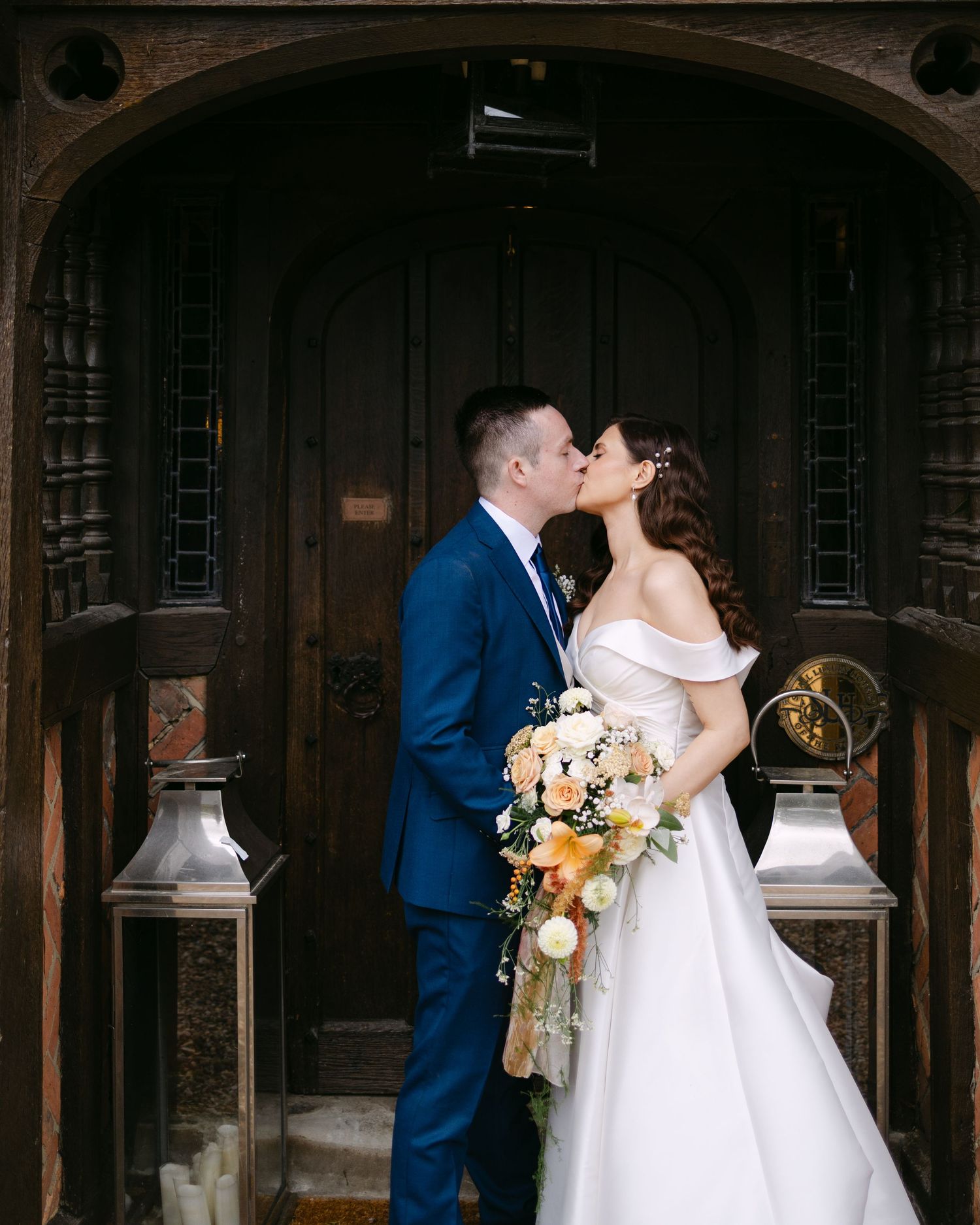 Romantic wedding moment captured outside historic Tudor-style building entrance.