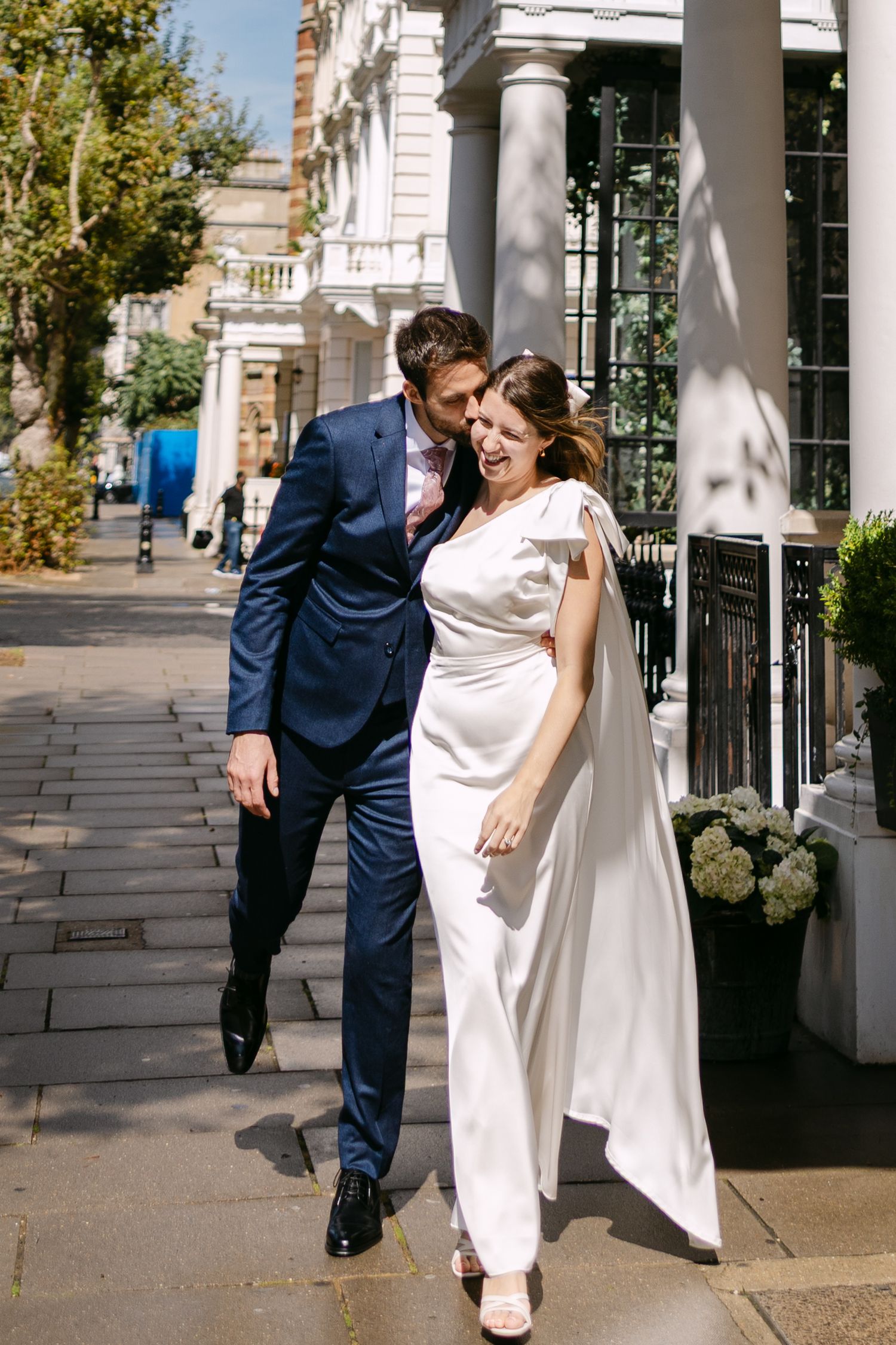 A wedding couple shares a playful moment together in a series of photos along a columned walkway.