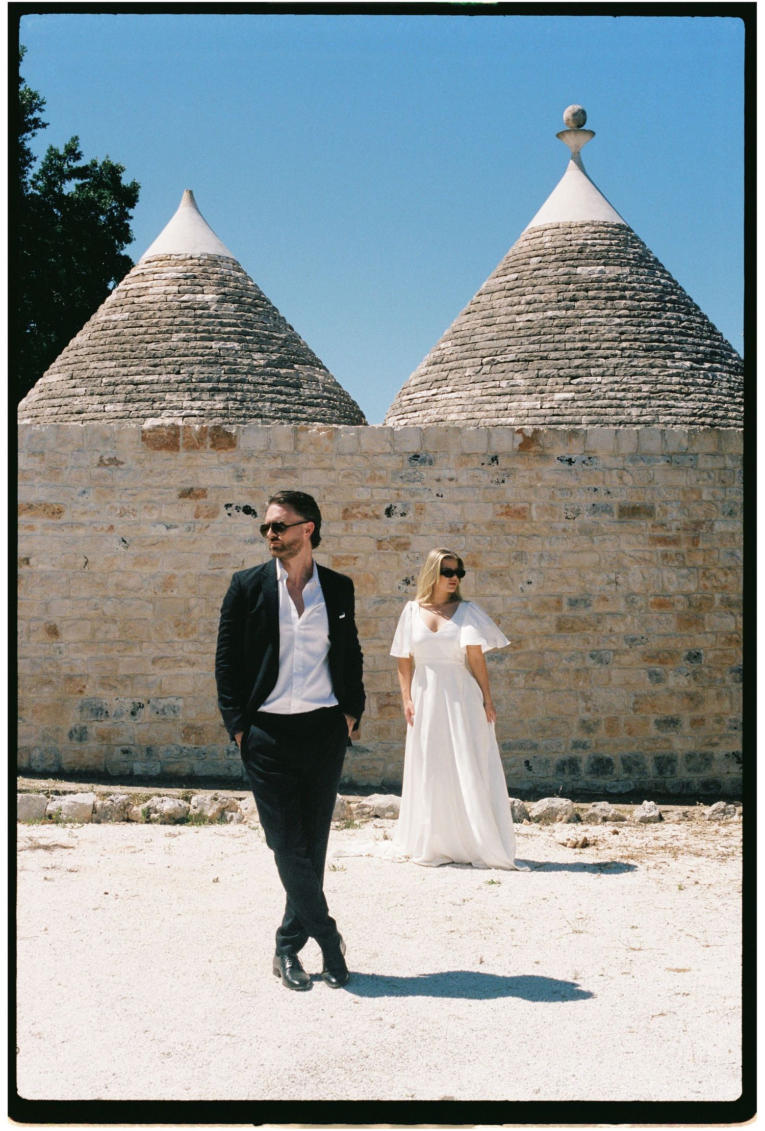 Bride and groom posing in front of traditional trulli stone buildings in Puglia, Italy.