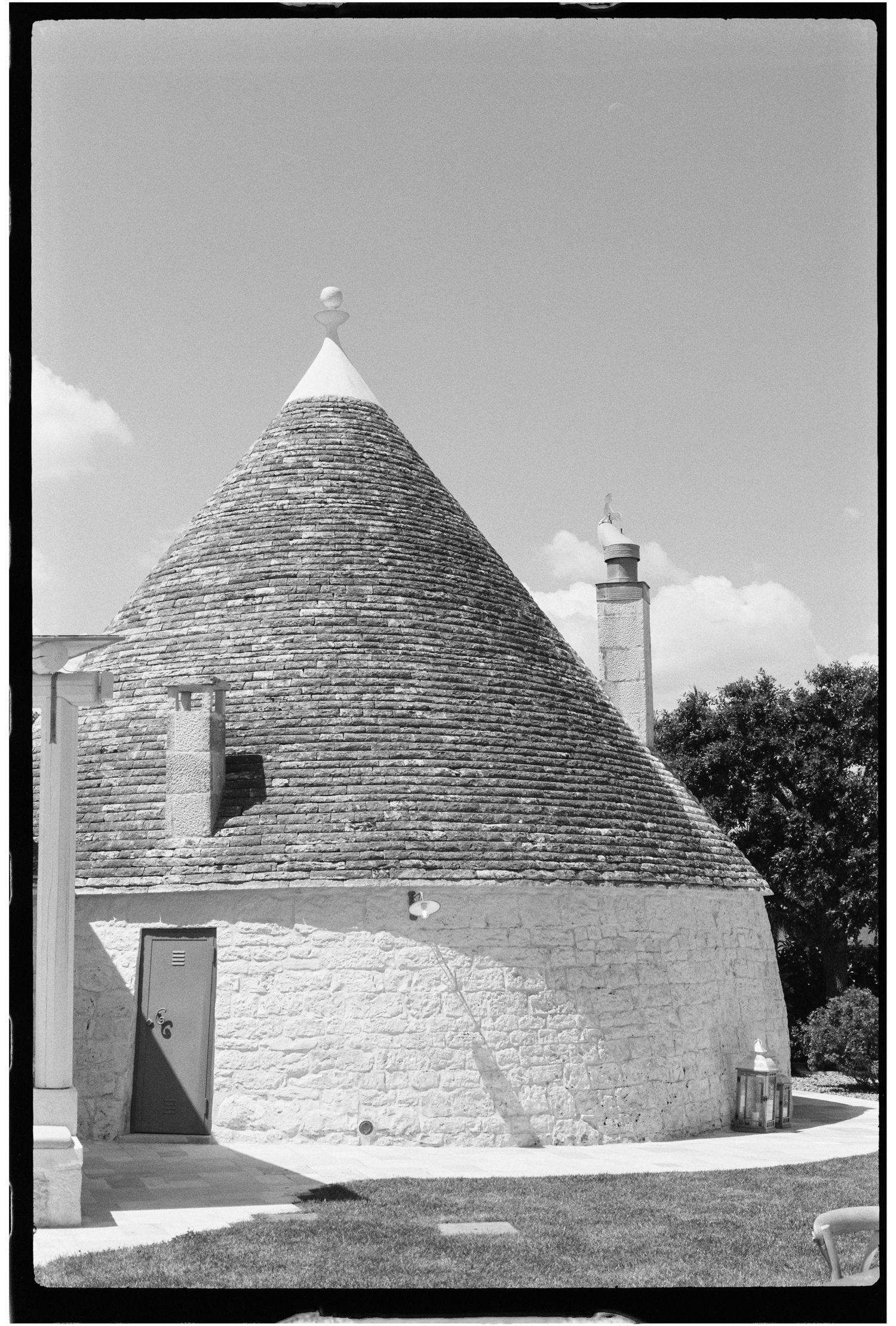 Black and white photo of a traditional Italian trullo stone building with conical roof and pinnacle in Puglia.