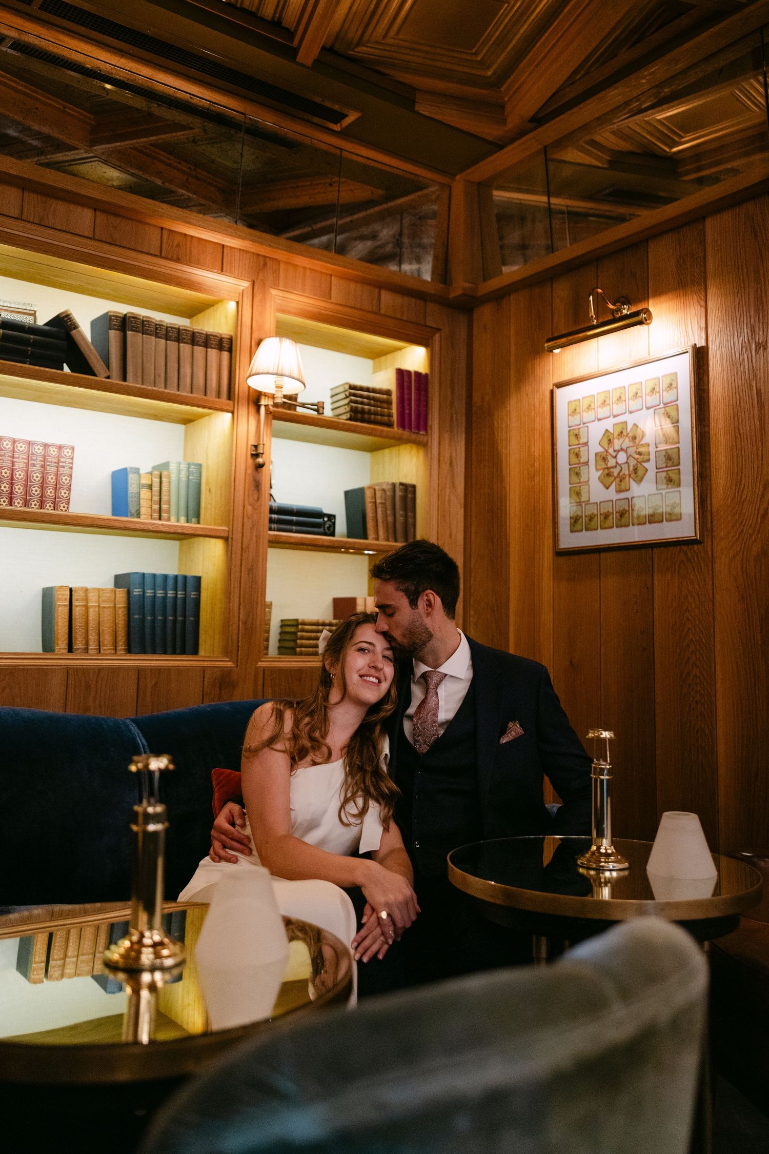 A cozy wood-paneled library setting with warm lighting creates an intimate atmosphere for a wedding photo at The Kensington Hotel.