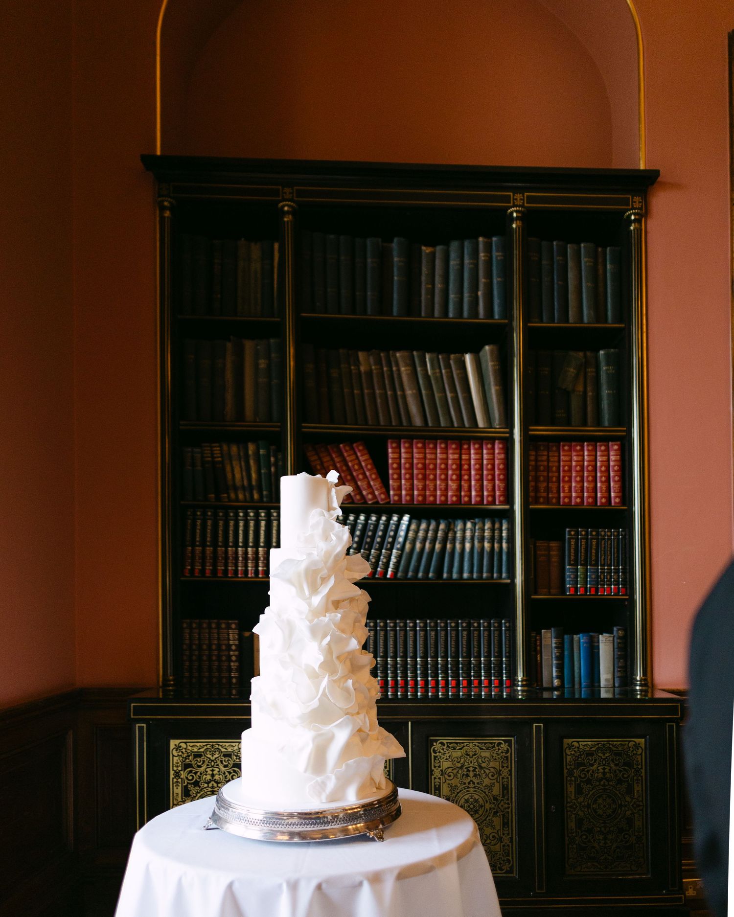 White wedding cake displayed in a library room with dark wooden bookshelves at Ashridge House, Hertfordshire.