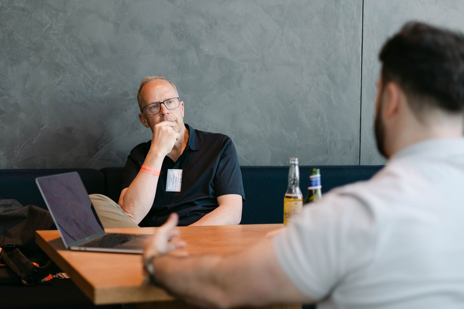 Two men having a business meeting at a wooden table with a laptop, book, and drinks in a modern office.