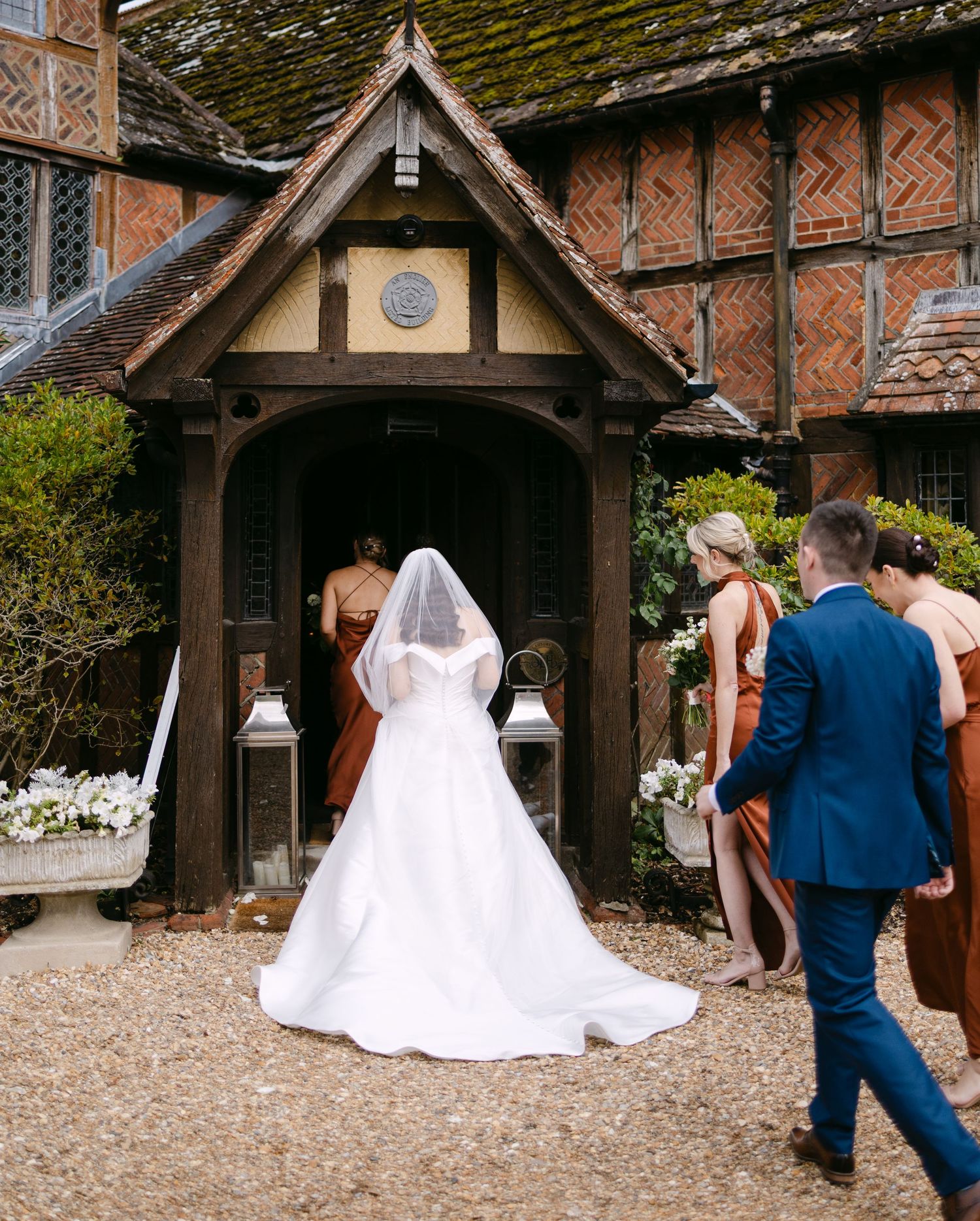 Wedding couple poses for photos outside a Tudor-style church entrance.