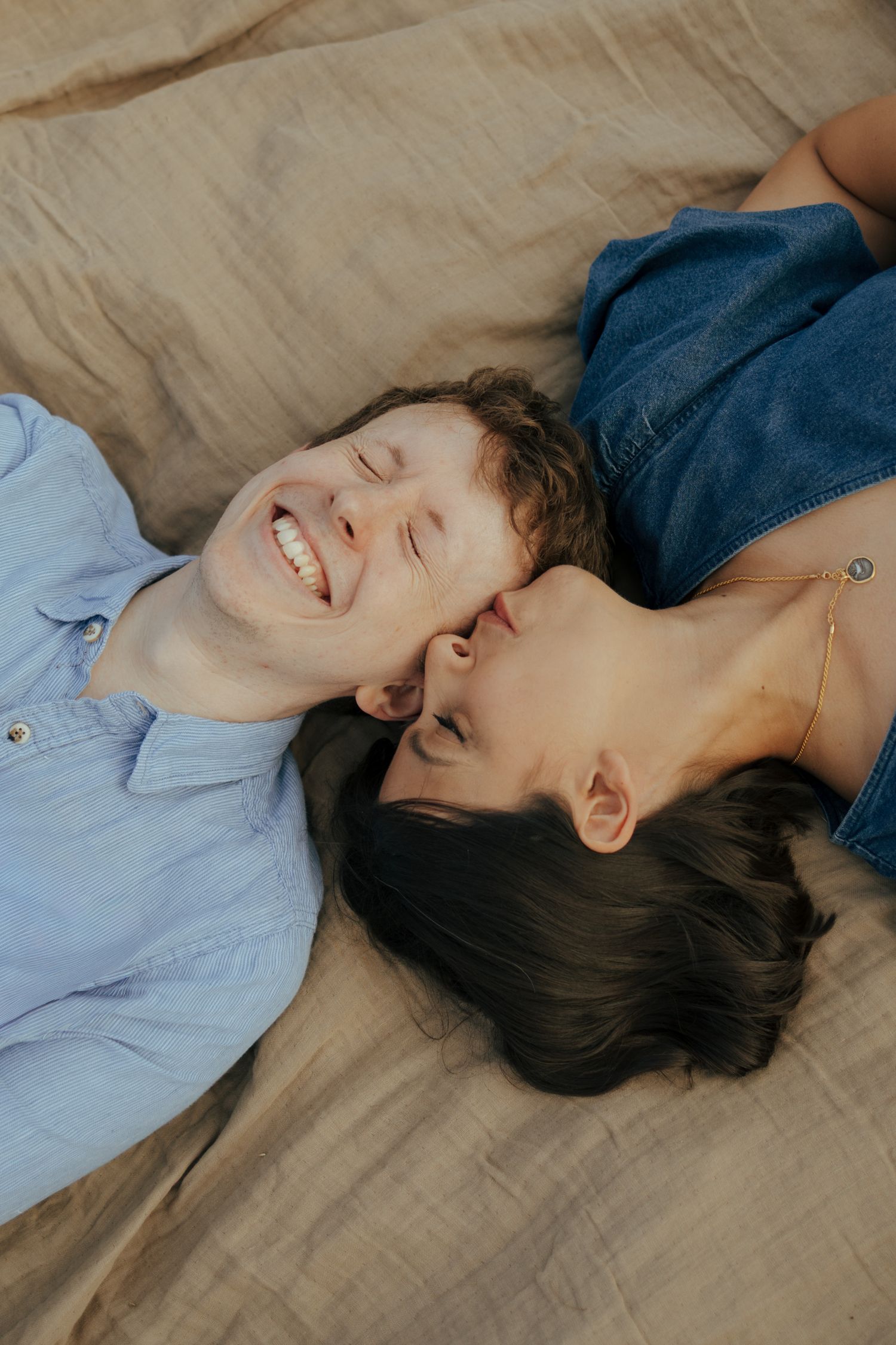 A couple lying on a beige blanket sharing intimate moments together.