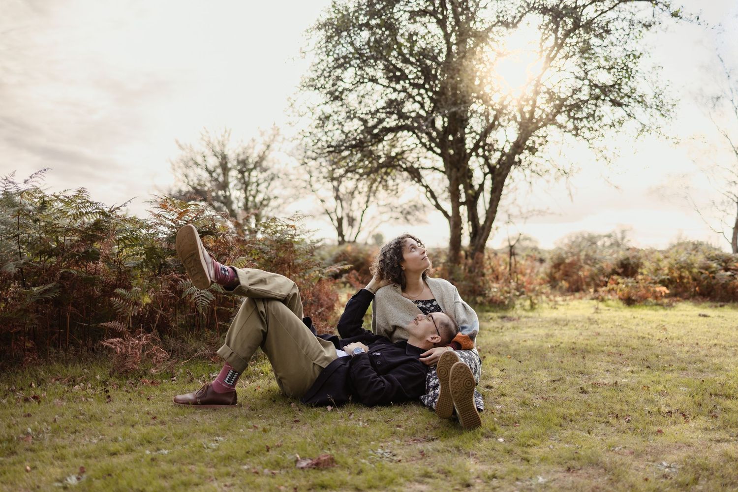 Couple lying together on grassy hillside during golden hour.