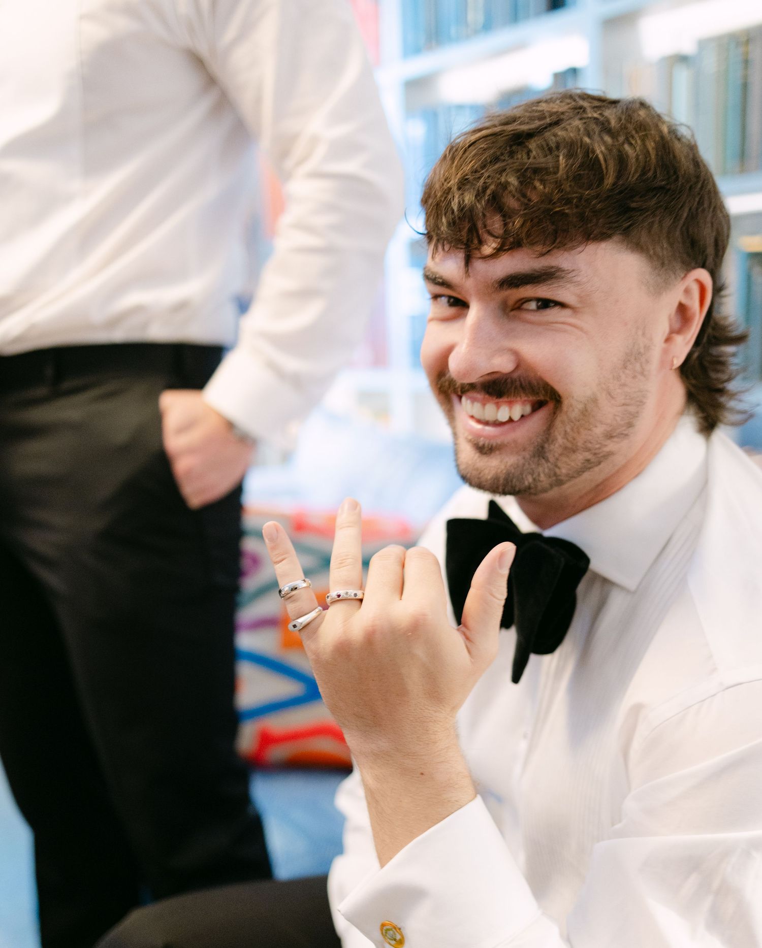 Groomsman in white dress shirt and black bowtie smiles while showing his rings.