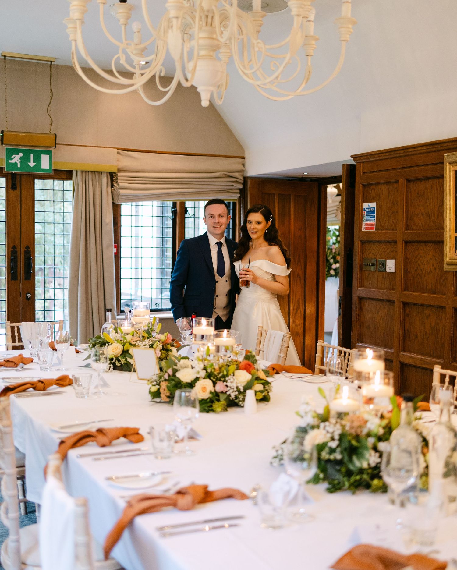 Elegant wedding reception room with chandeliers and tables set with floral centerpieces.