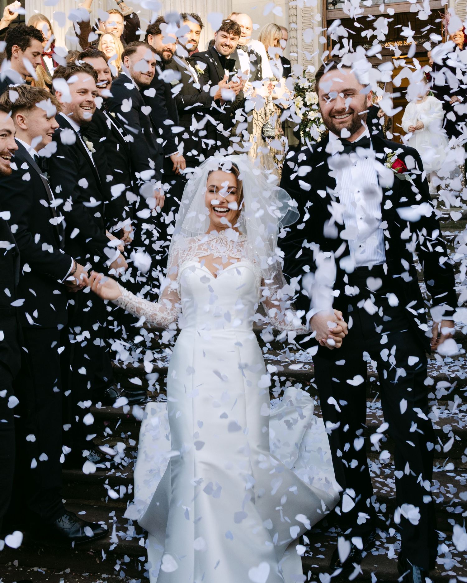 Joyful wedding celebration with white confetti shower against dark background.