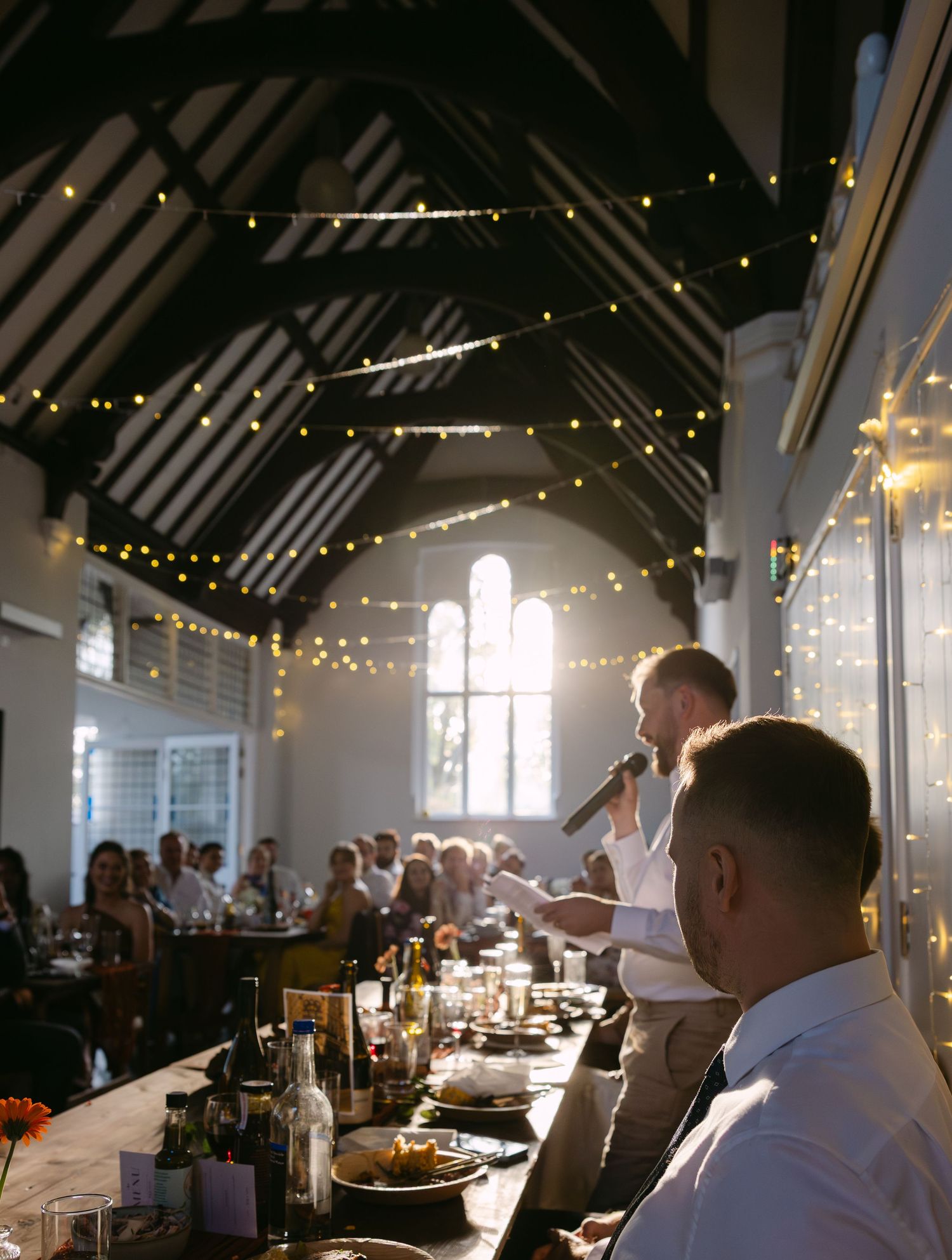 Interior of a grand hall with exposed beams and string lights during a wedding reception.