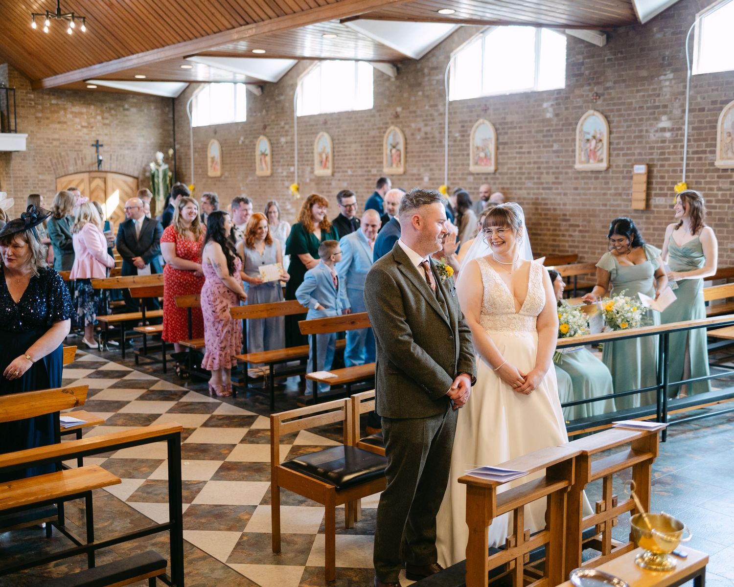 Bride and groom stand at church altar during wedding ceremony with guests seated in pews of a brick church.