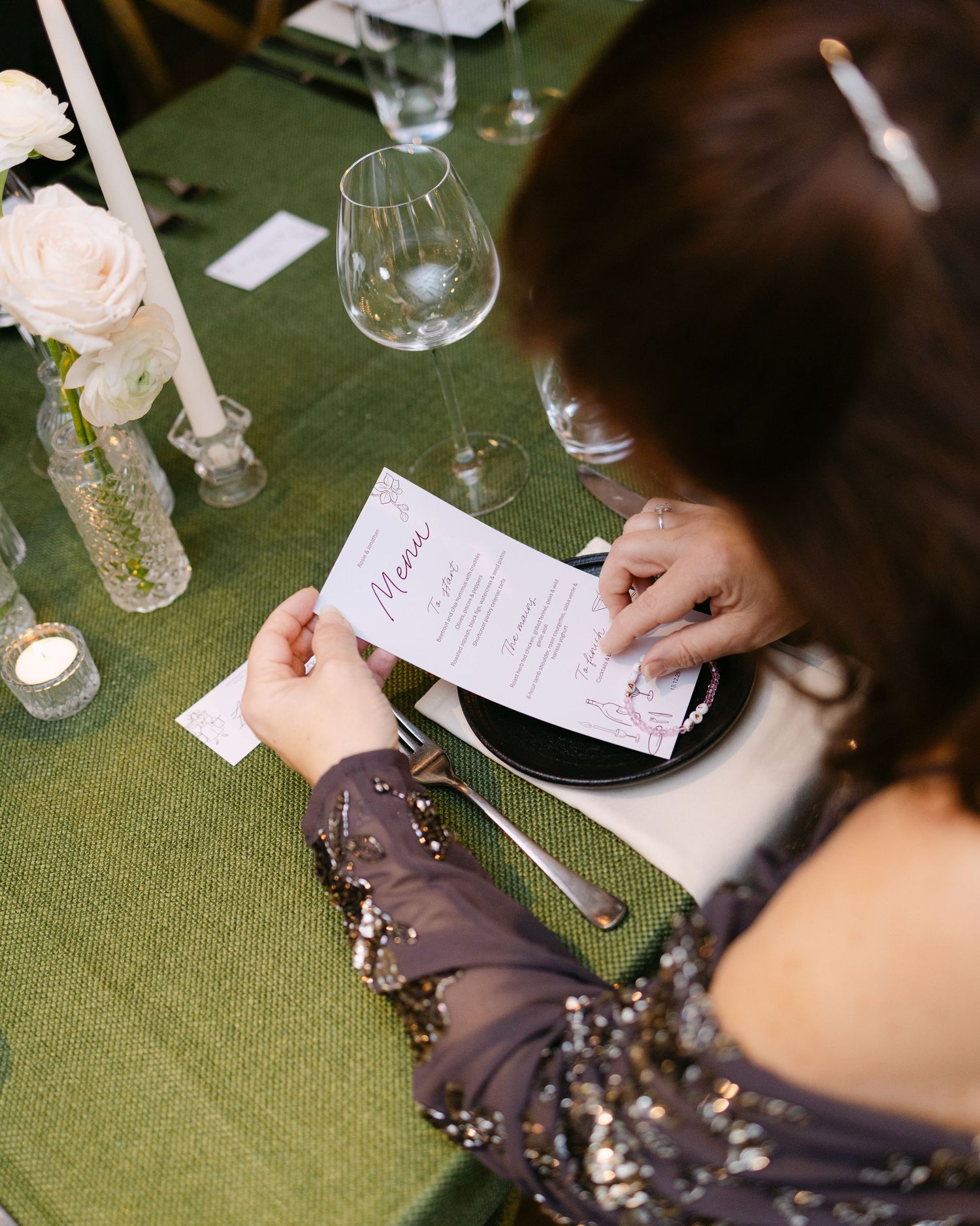 Wedding guest reading menu cards at an elegantly set table with green tablecloth.