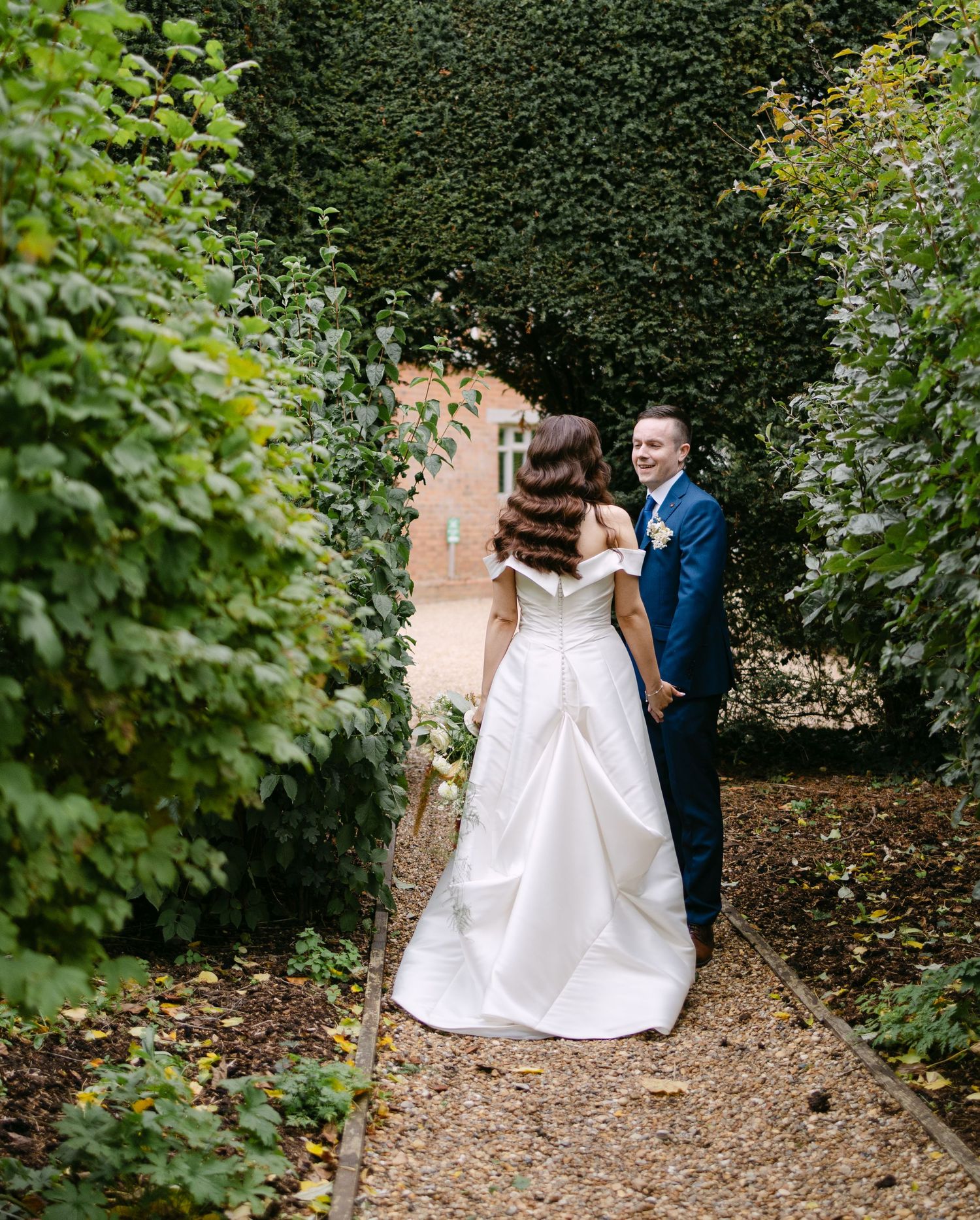 Wedding couple walking along a garden path surrounded by lush greenery.