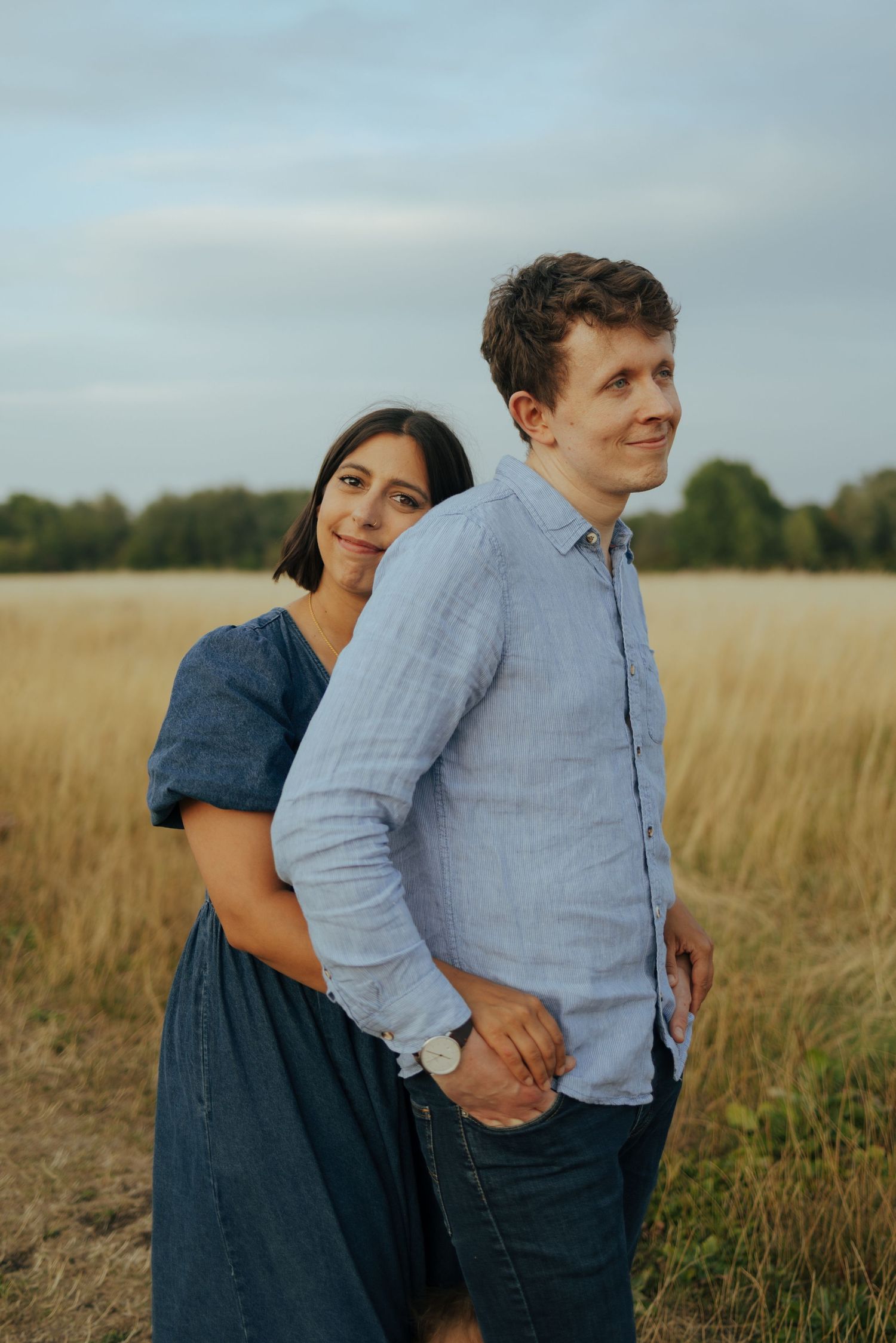 A couple poses playfully together in a golden grass field during late afternoon.