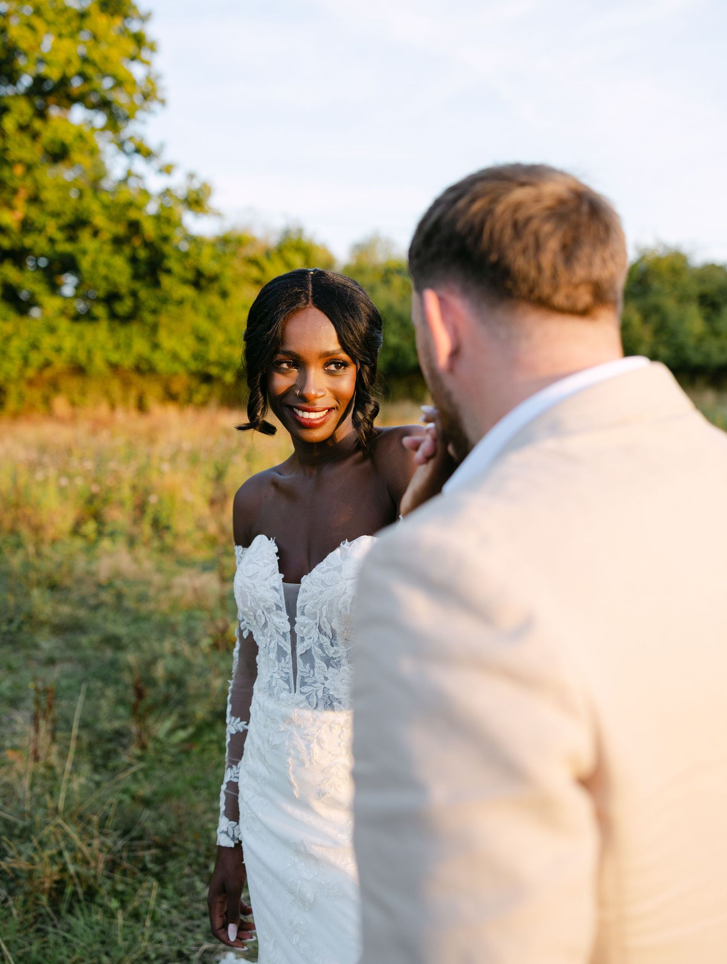 A couple enjoys a playful moment in a grassy field during their wedding photoshoot.