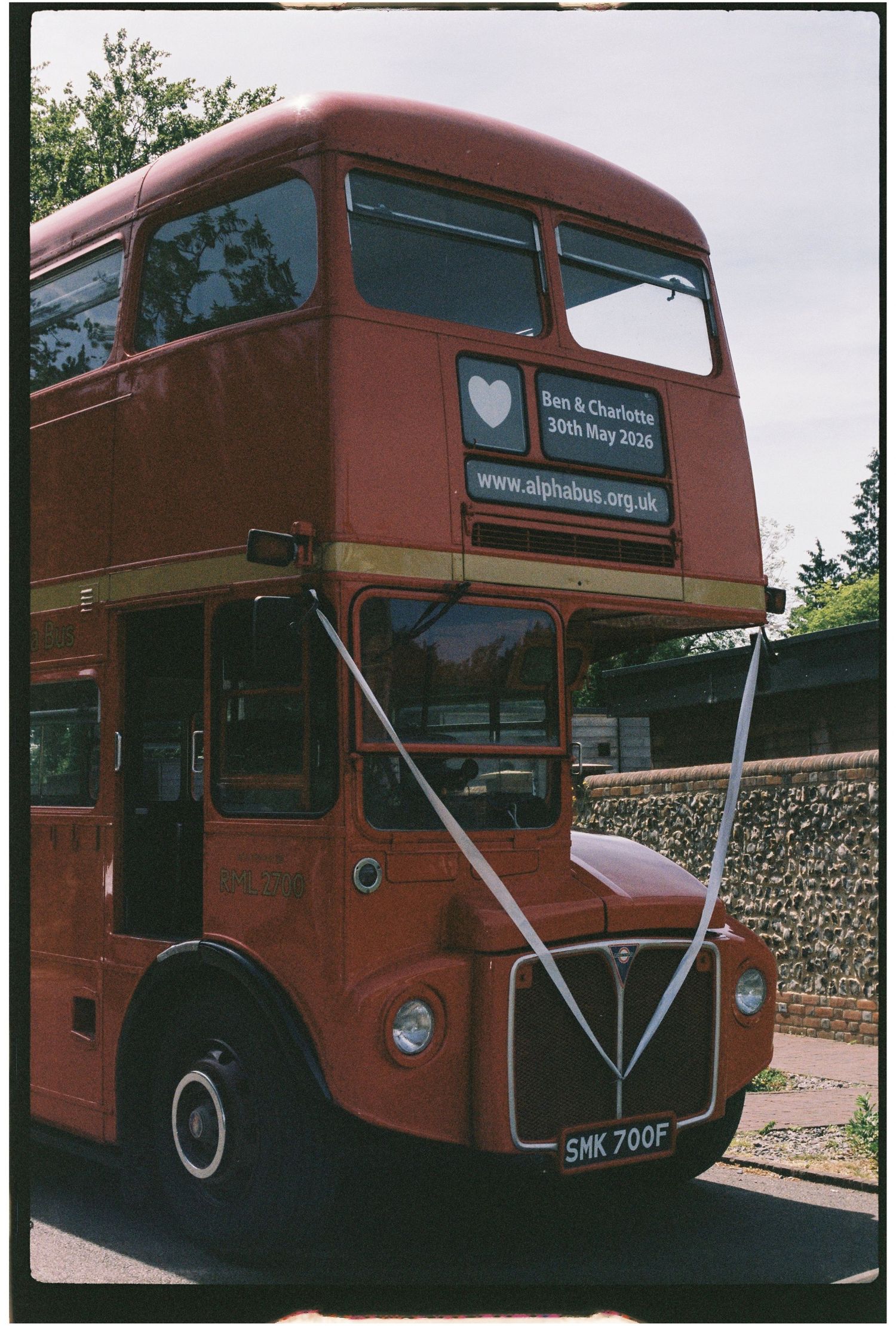 Classic red double-decker London bus decorated with white ribbons for Ben and Charlotte's wedding, 30th May 2026.