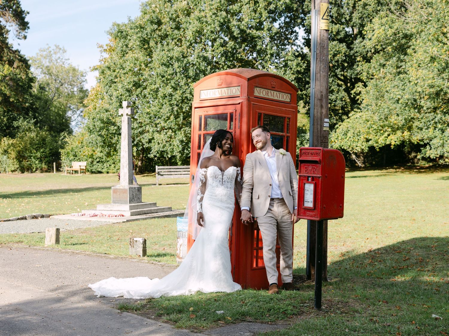Wedding couple posing near a classic red British phone booth in a garden setting.